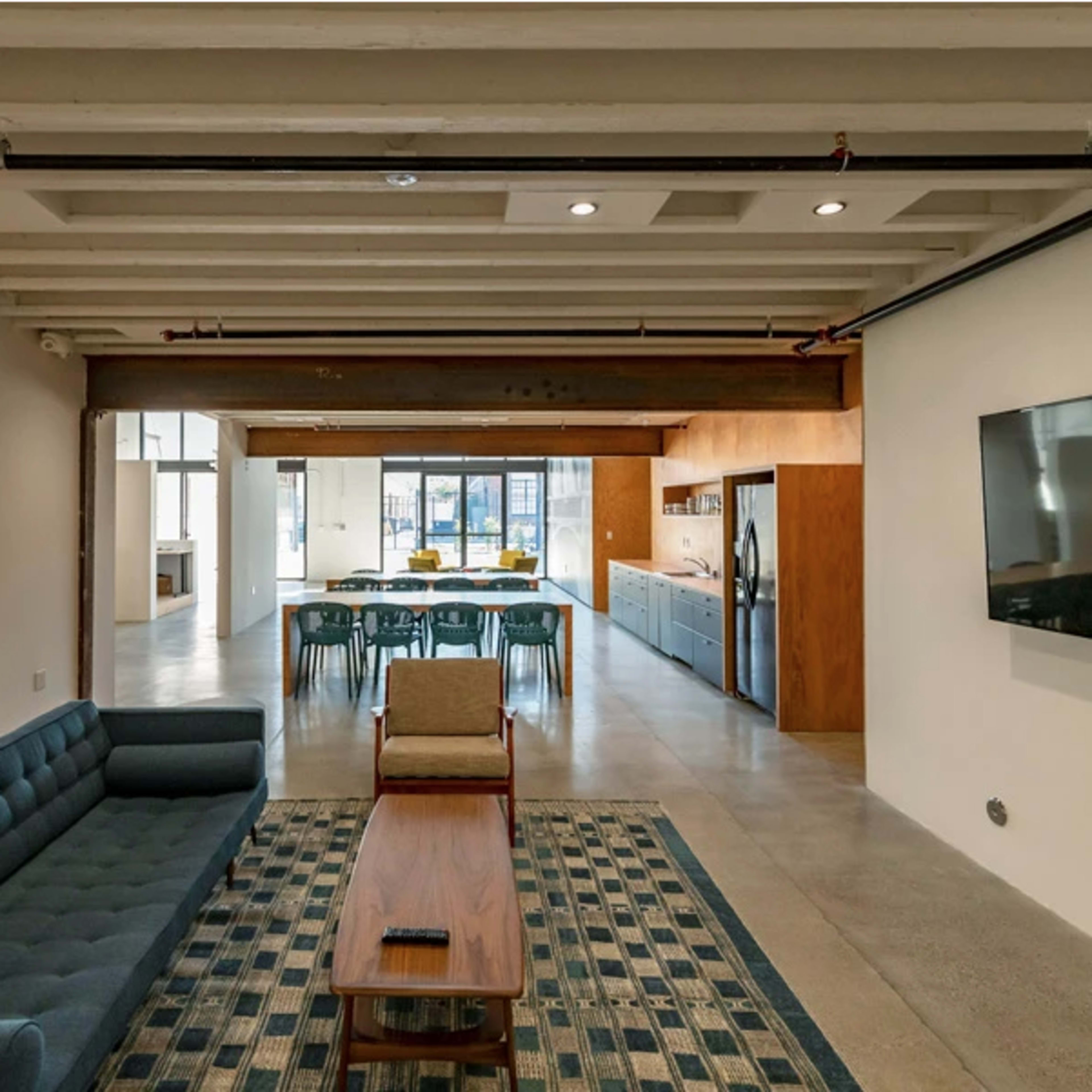A modern open-concept living space featuring a blue sofa, wooden coffee table, and a dining area with a long table and chairs in the background.