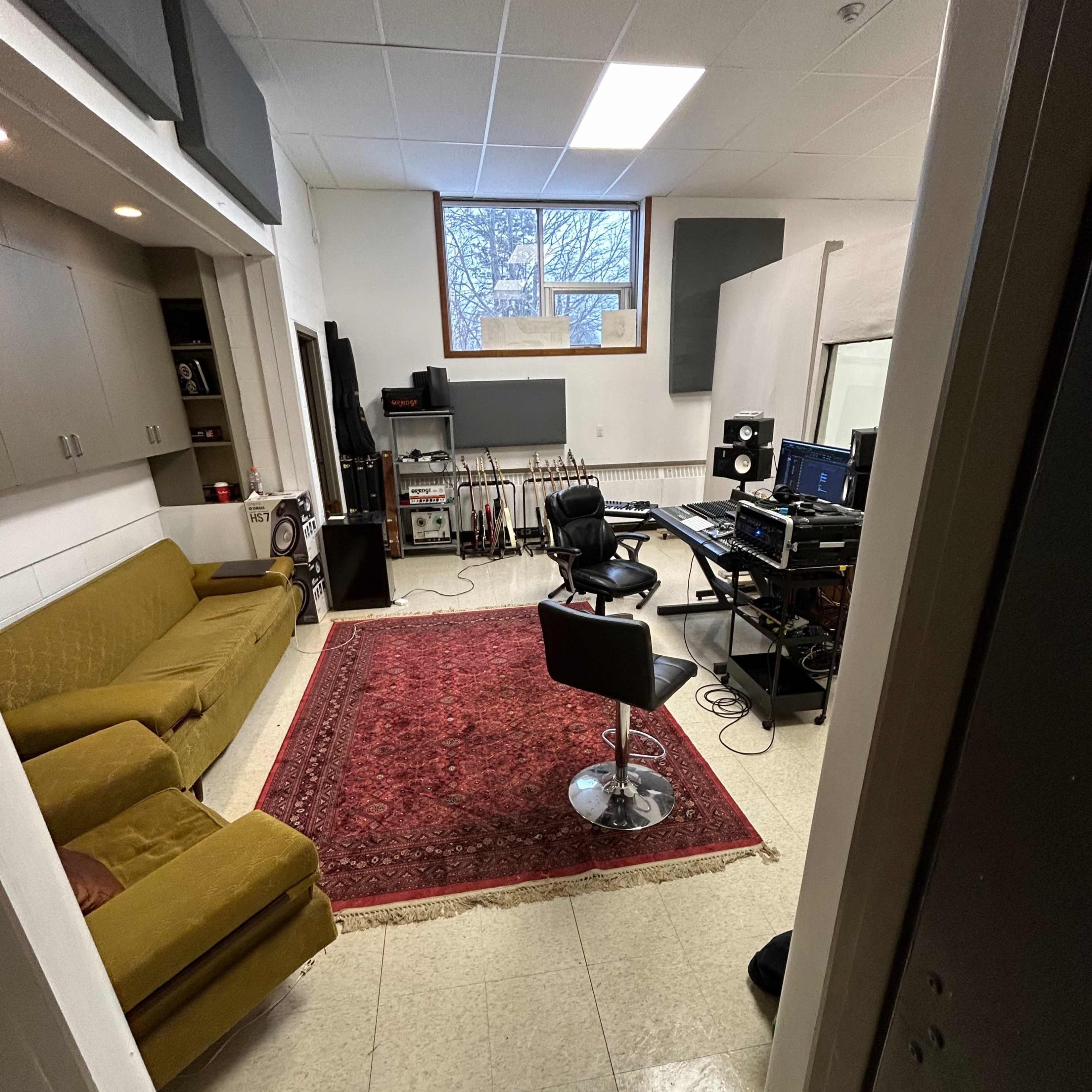 A recording studio with a green sofa, a red area rug, and a workstation equipped with audio equipment and a chair.