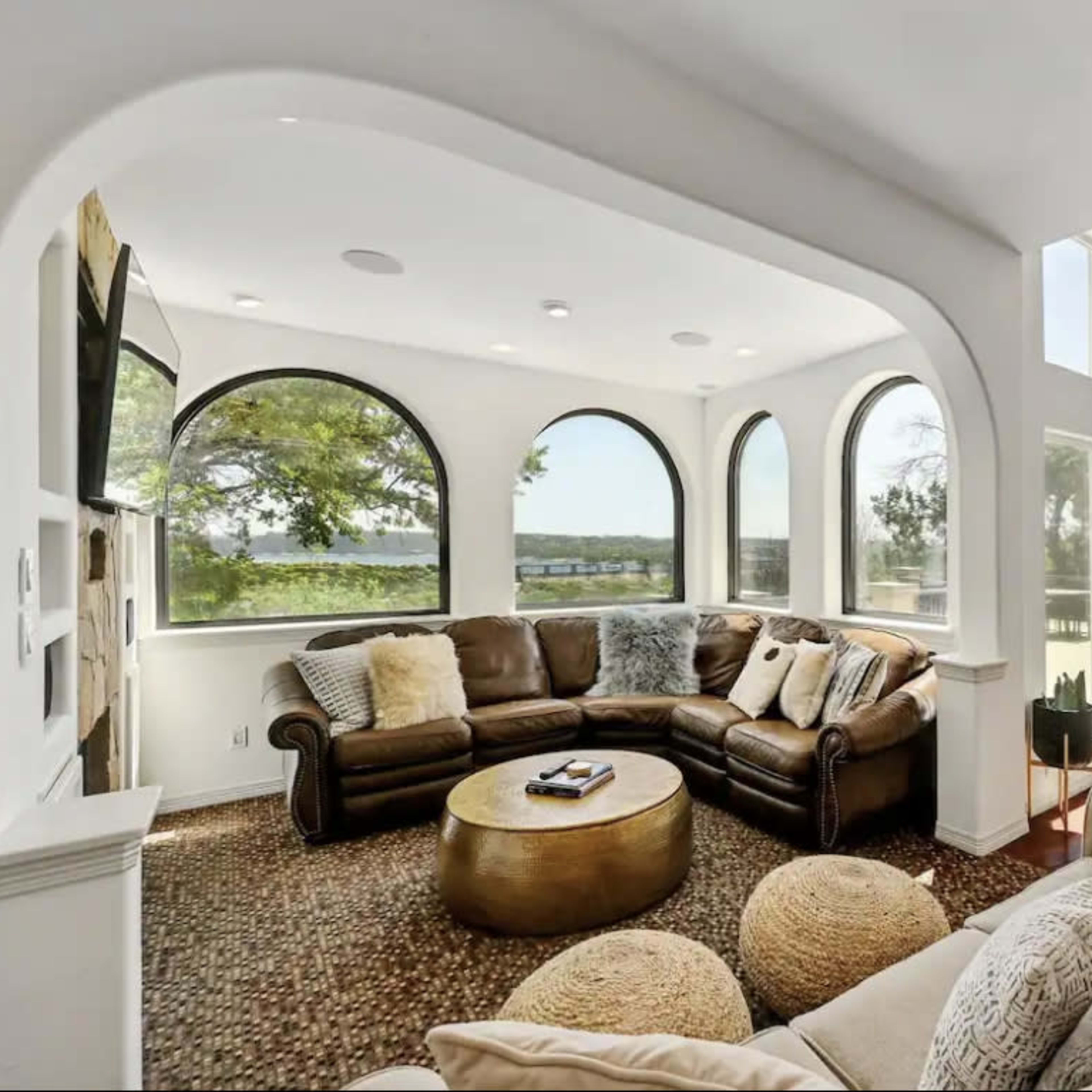 A spacious living room with large arched windows, two seating areas, and a view of a landscape outside.