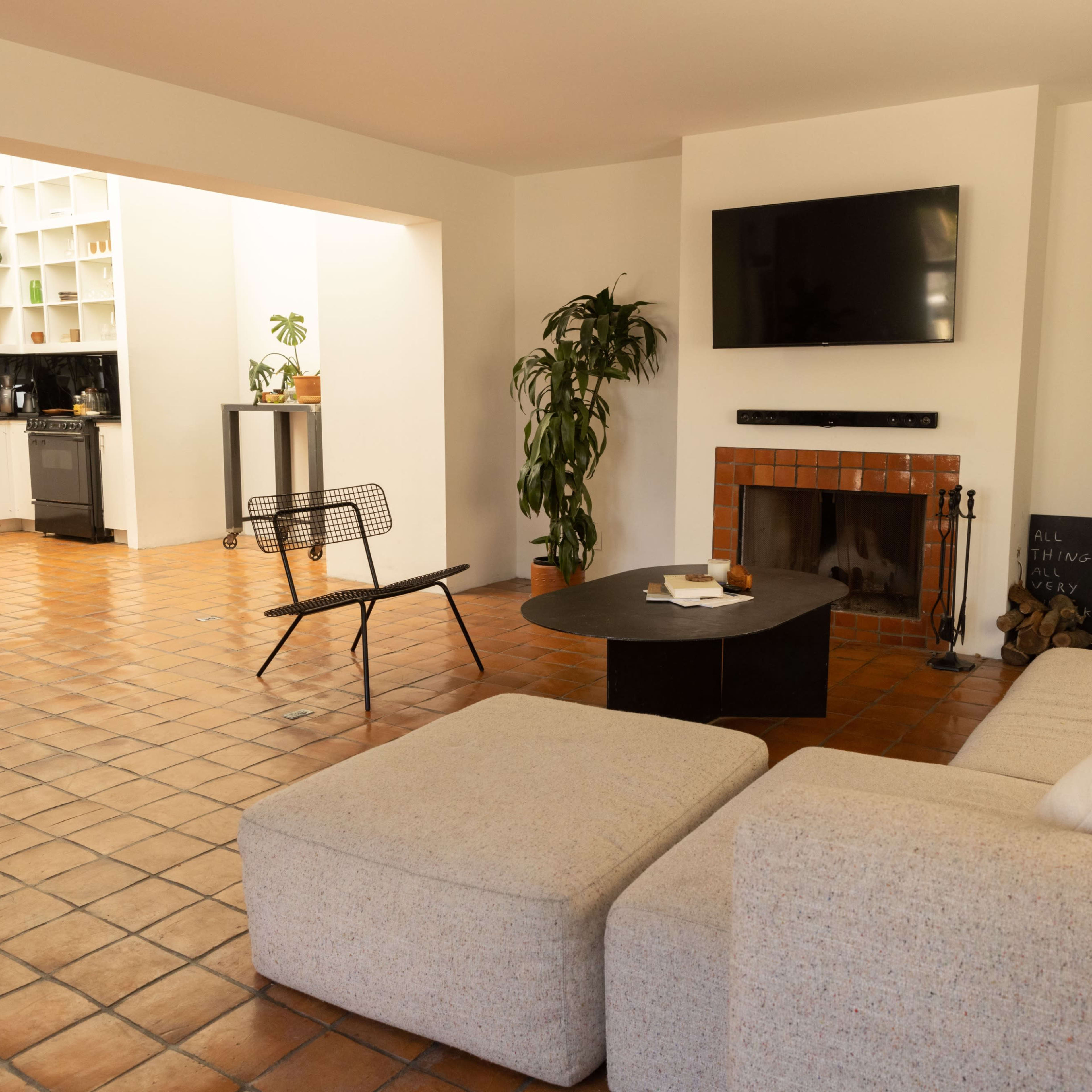 A spacious living area features a sectional sofa, a round coffee table, a fireplace, and a view into a kitchen with a black countertop and white cabinetry.