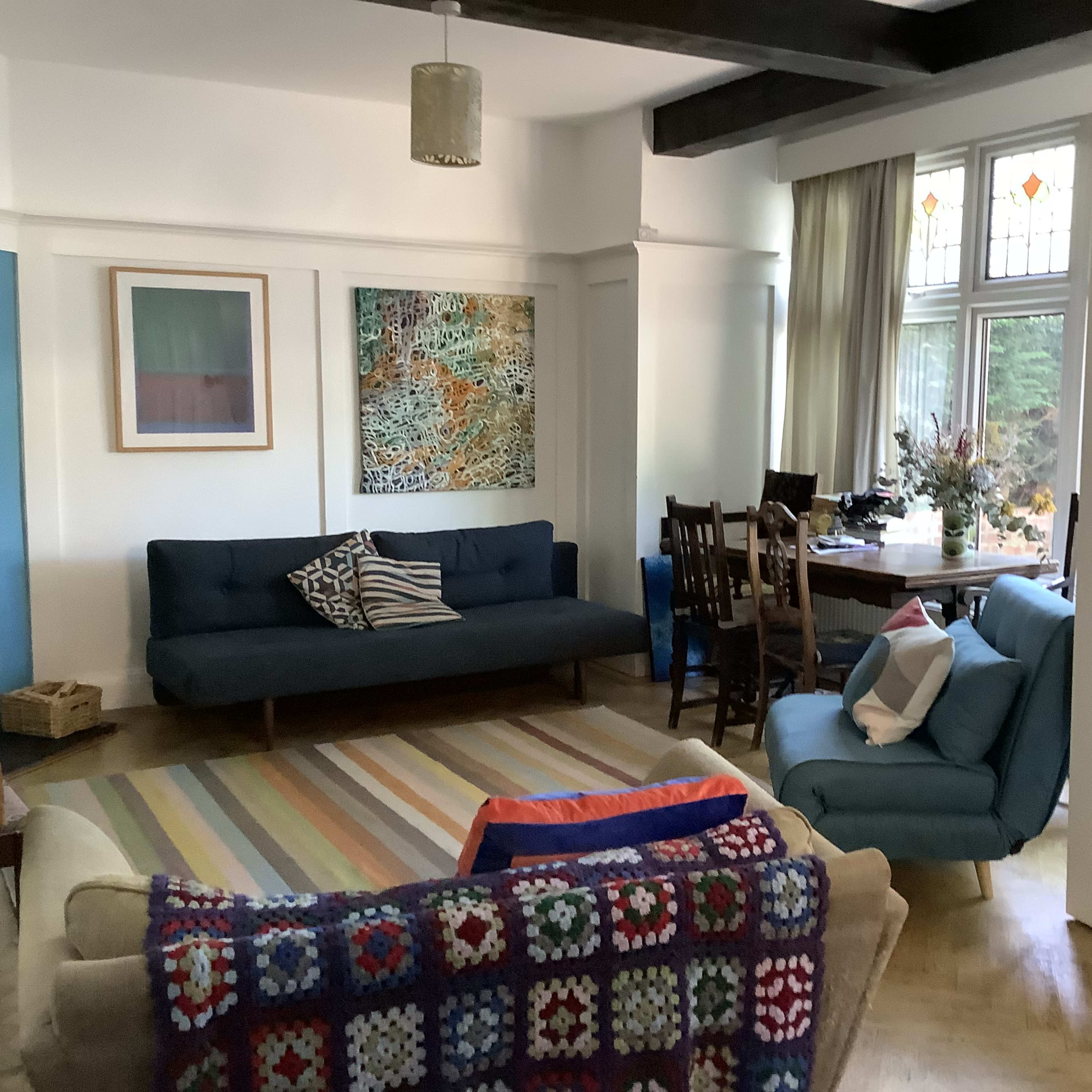 A cozy living room with a blue sofa, a light-colored armchair, a patterned rug, and a dining table set for several people.