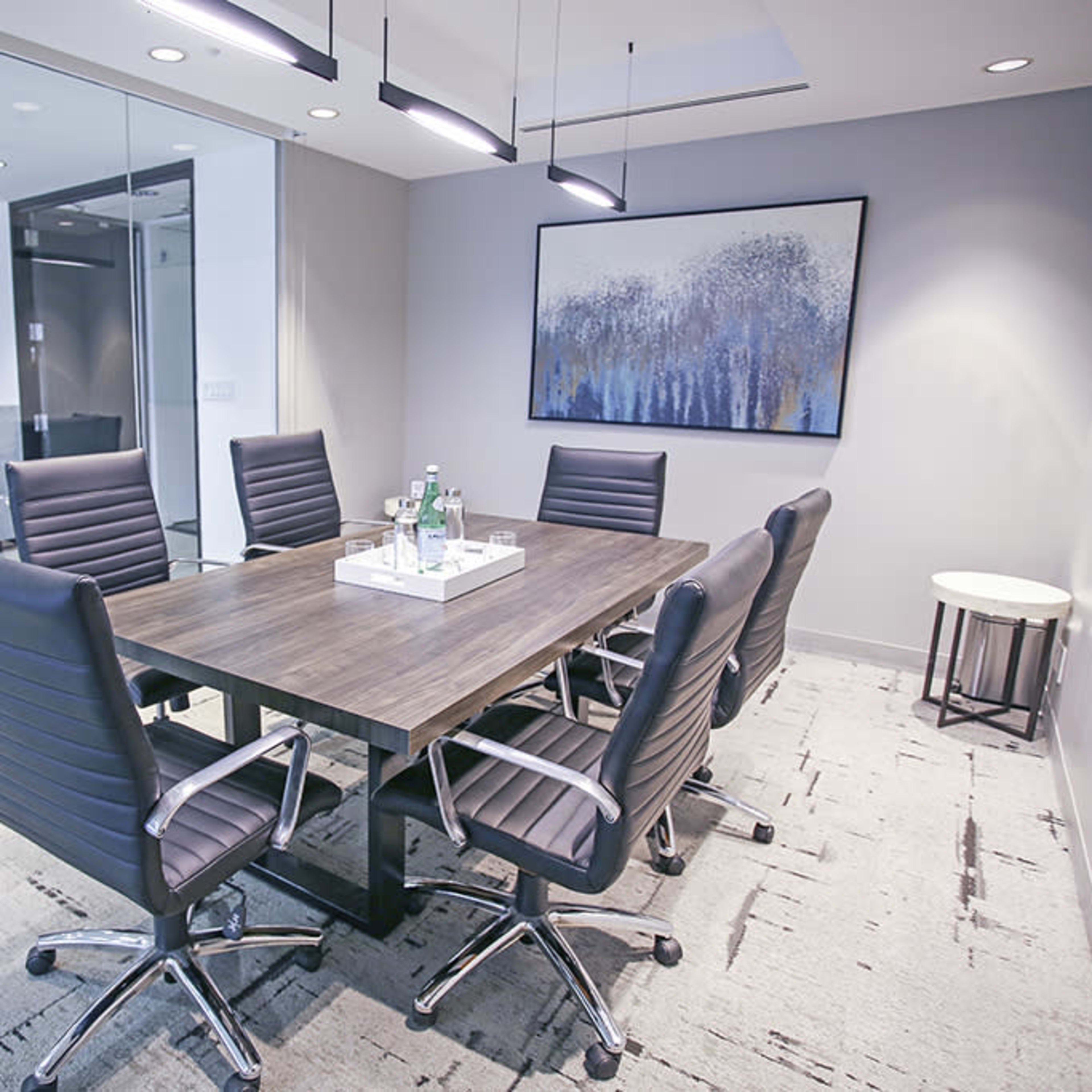 A modern conference room features a large wooden table surrounded by black ergonomic chairs, with glass walls offering a view of an adjacent space.