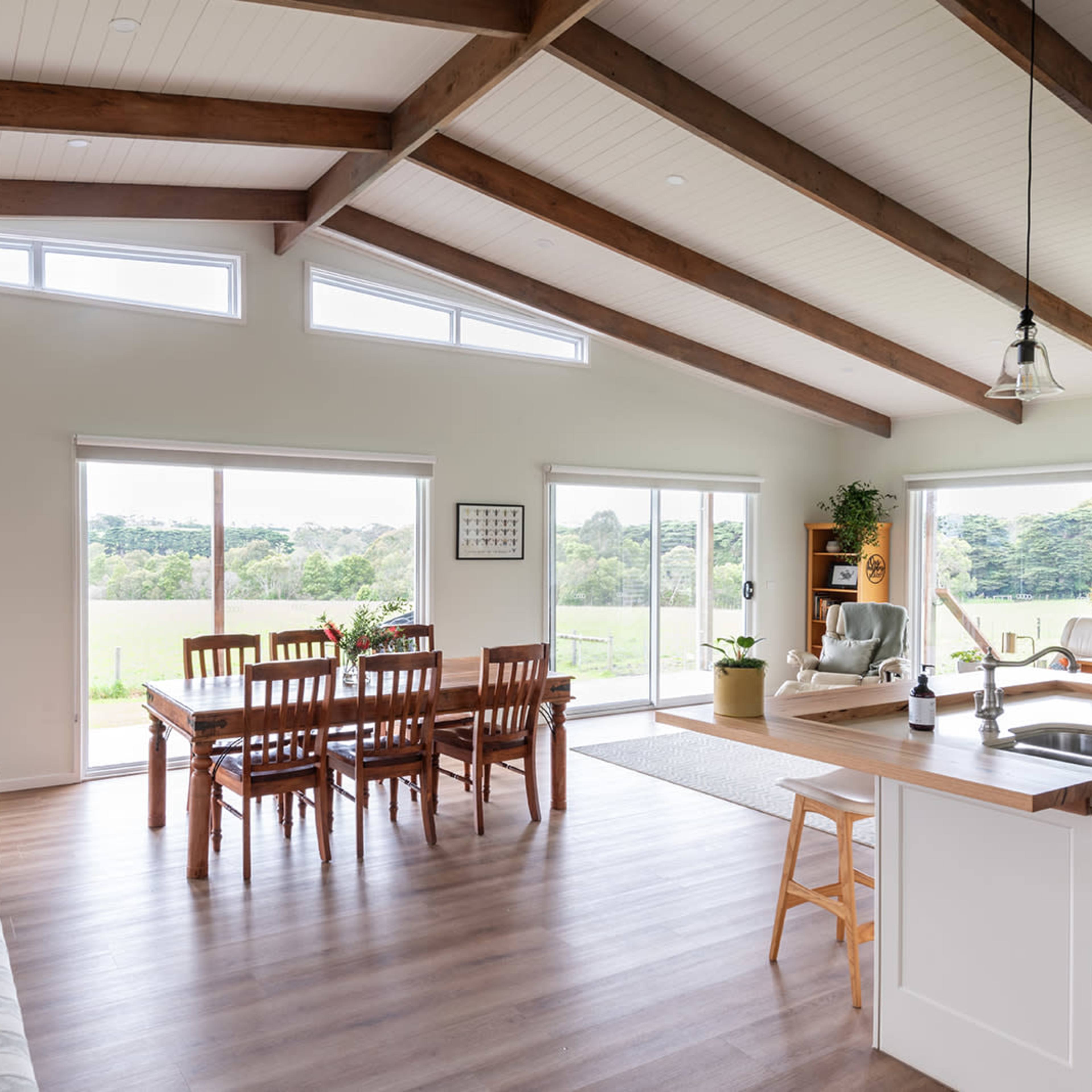 The open-concept living area features a dining table, kitchen island, and large windows overlooking a green landscape.