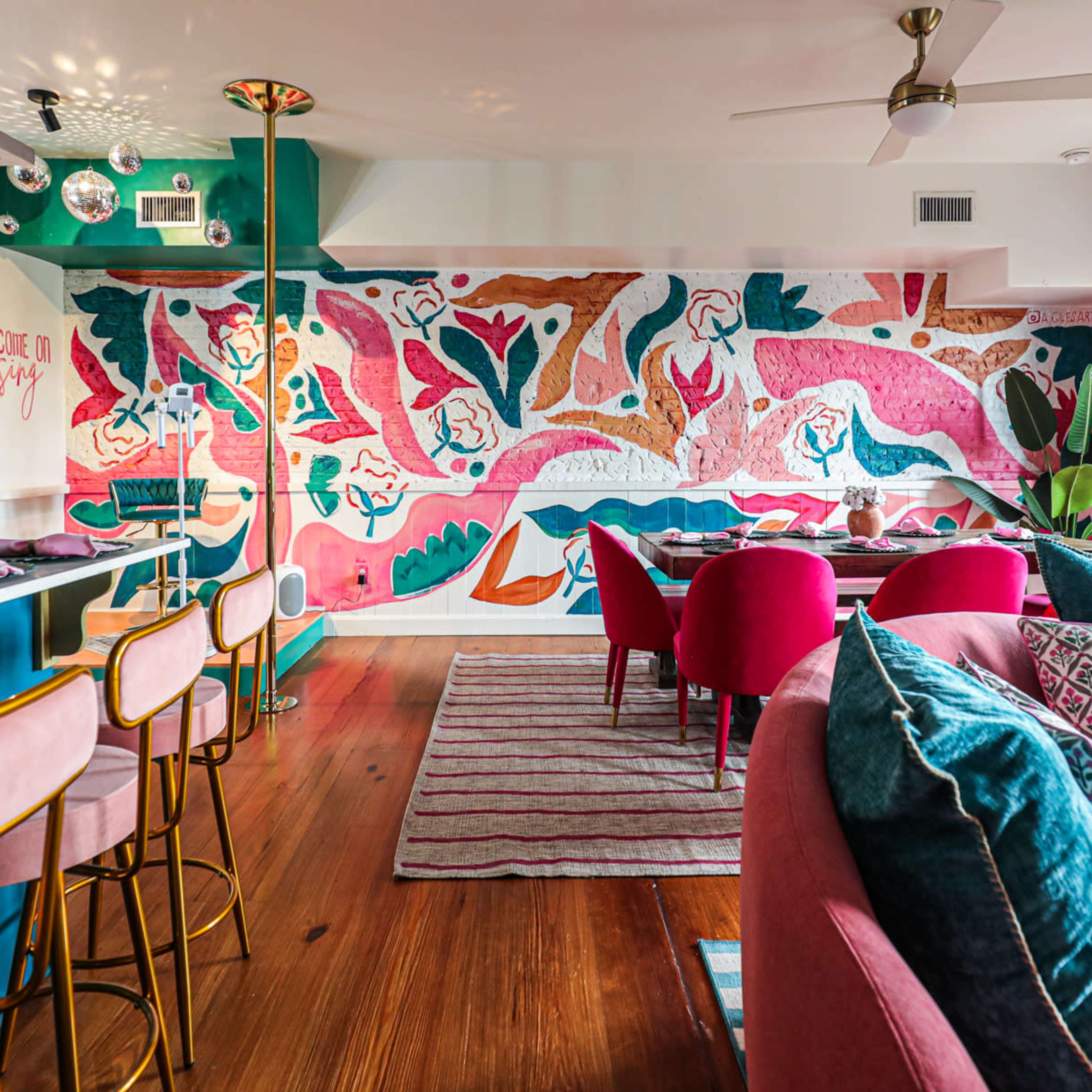 A colorful, modern interior space featuring a vibrant mural, stylish seating, and a bar with golden accents.