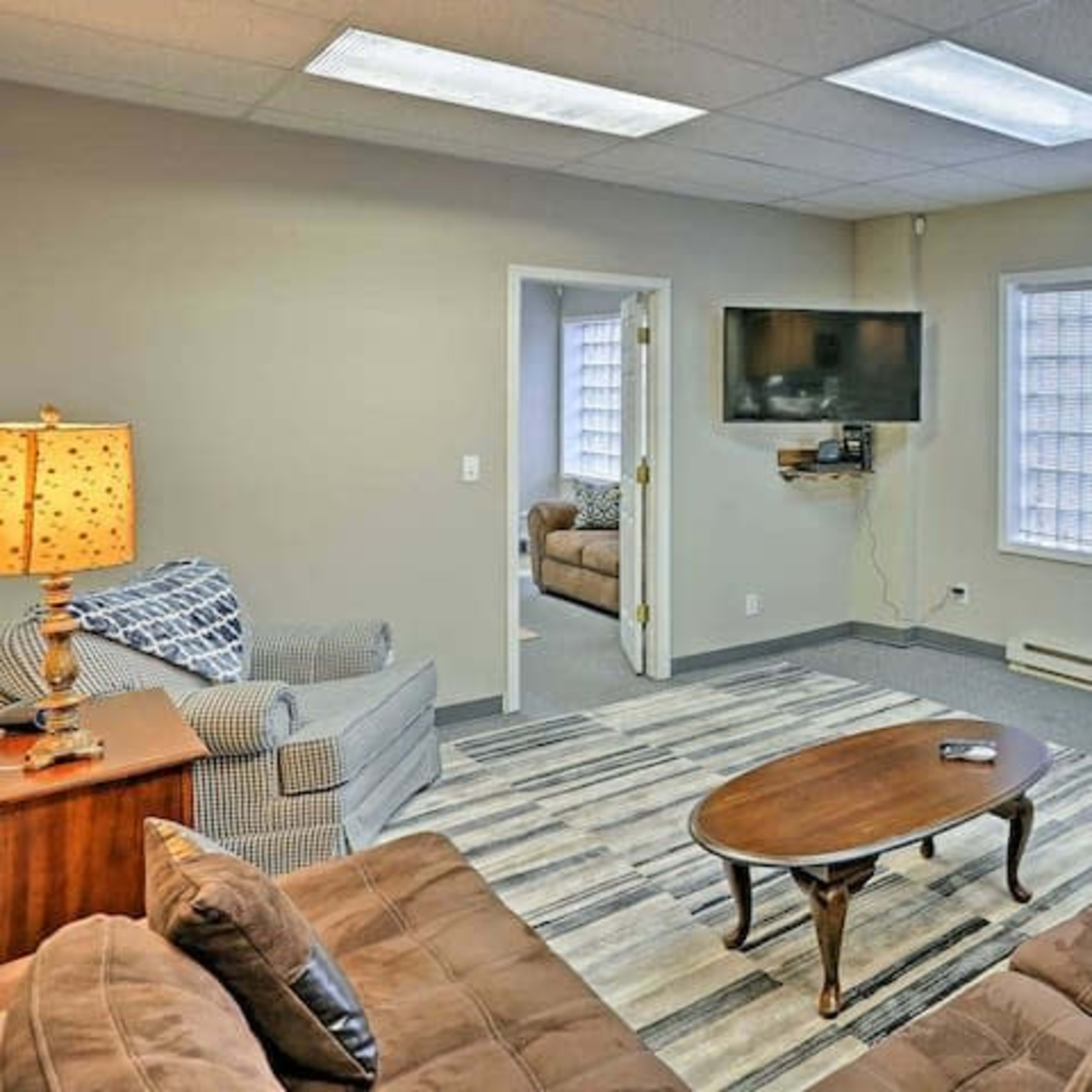 A well-furnished waiting room with two sofas, a coffee table, and a television mounted on the wall.