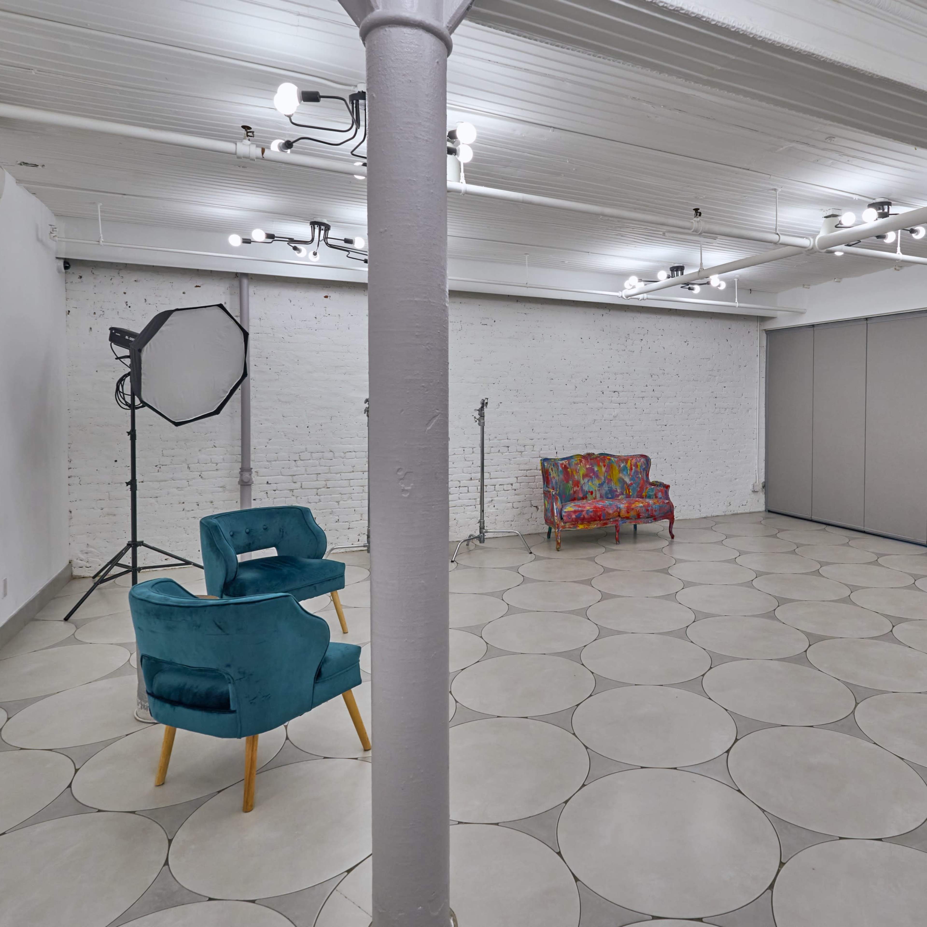 A spacious room with a patterned tile floor, two chairs, a photography light setup, and movable partition panels against a white brick wall.
