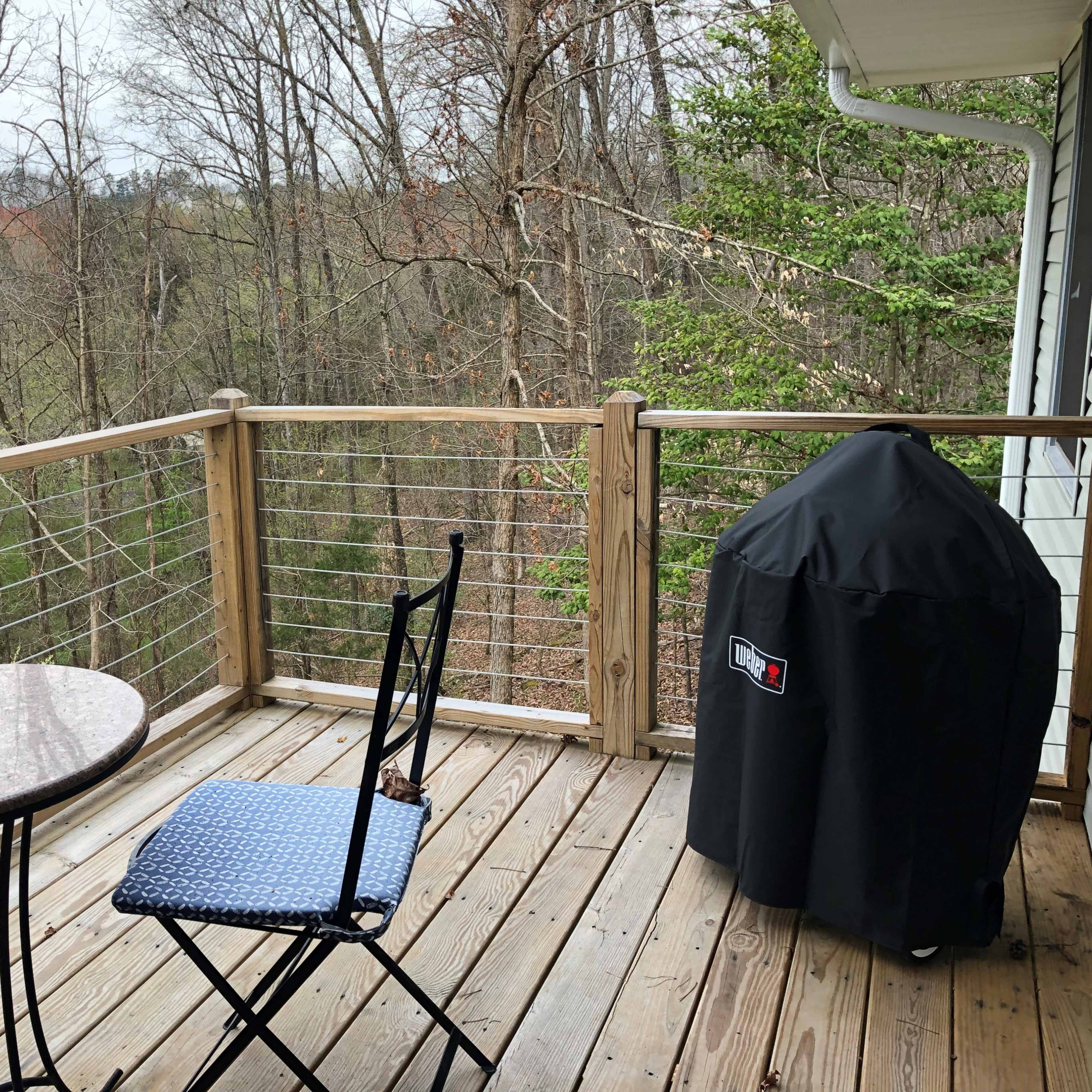 A small wooden balcony with a round table and two chairs, overlooking a wooded area.