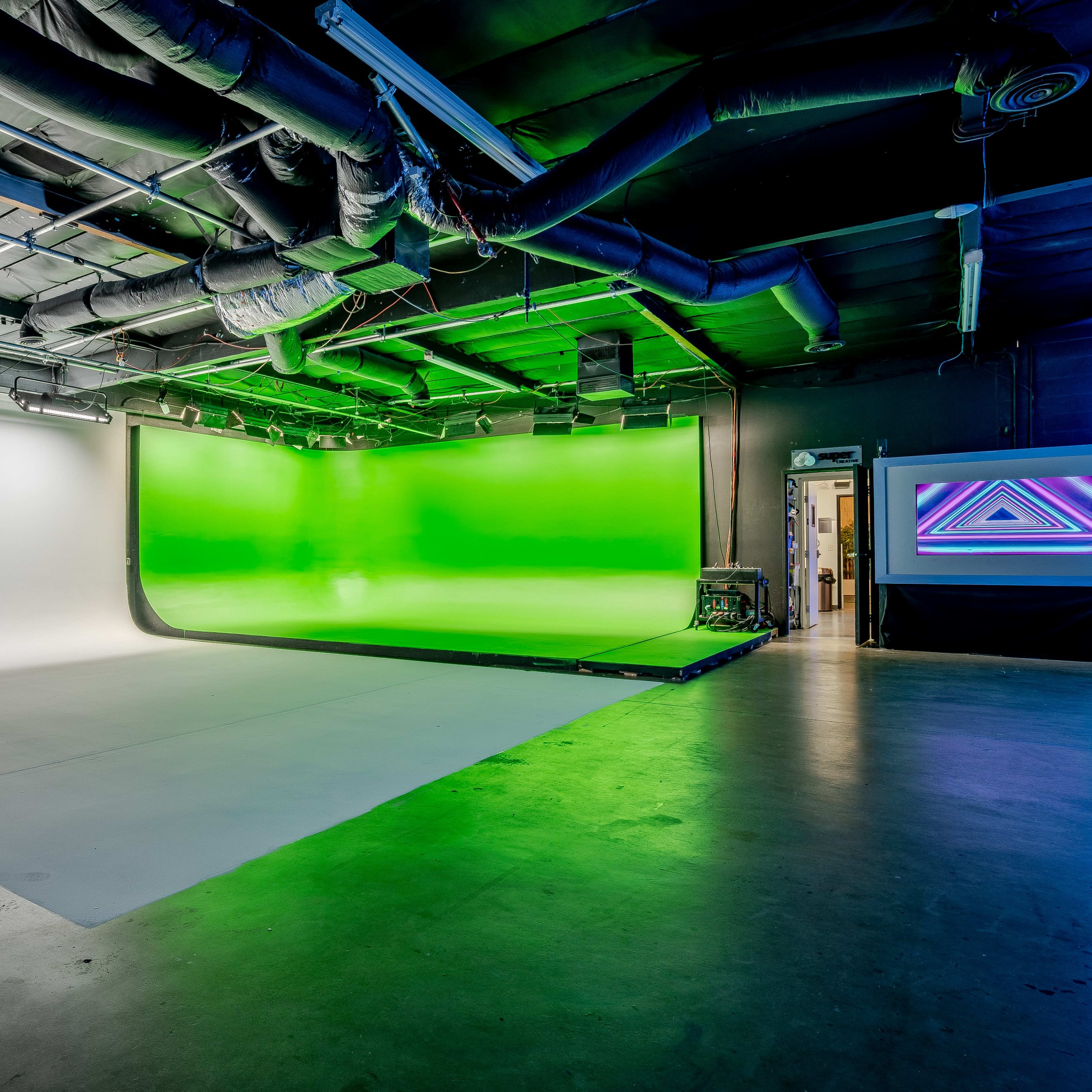 A studio space with a white backdrop on one side and a green screen on the other, highlighted by various lighting installations.
