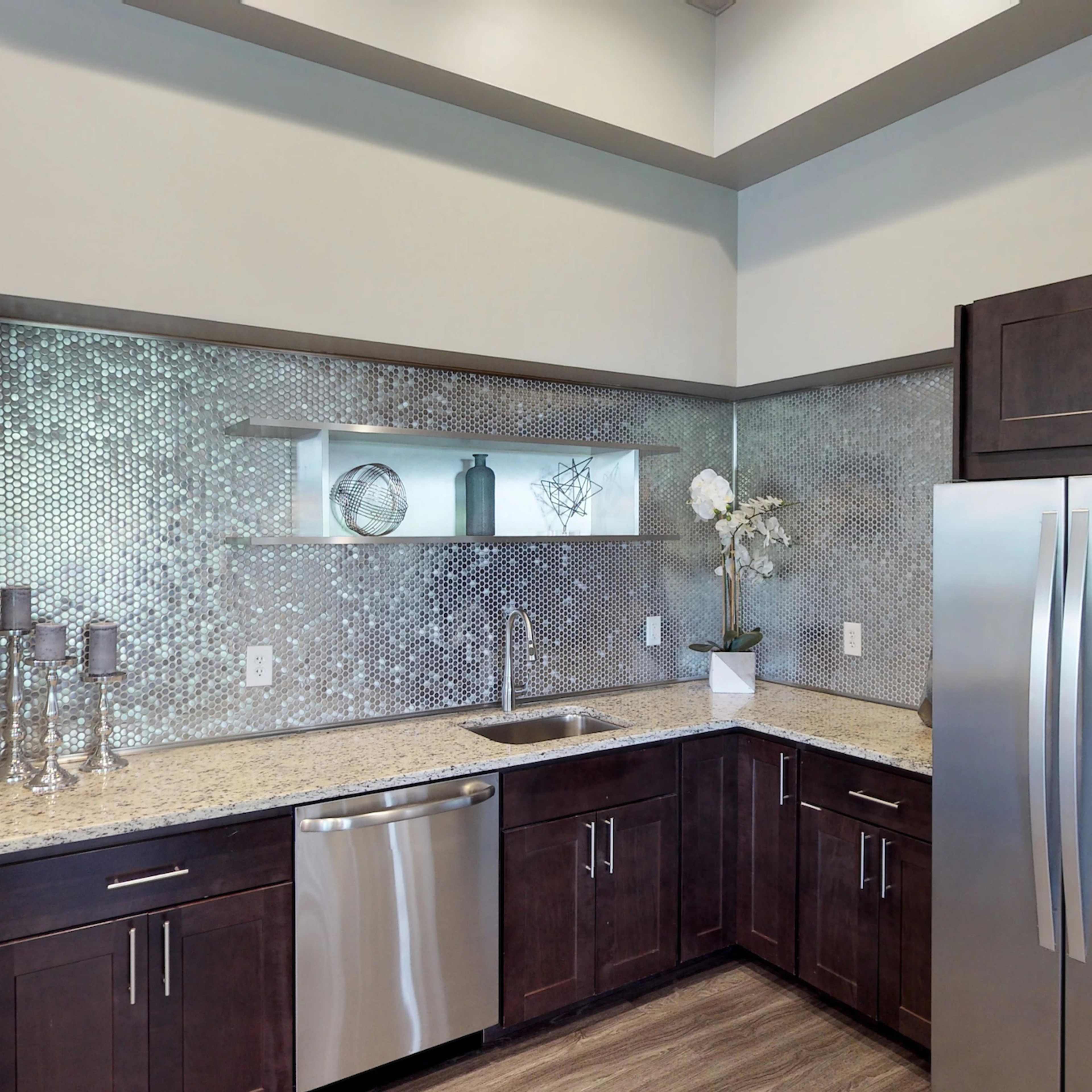 A modern kitchen features dark wooden cabinets, a stainless steel refrigerator, and a backsplash with mosaic tiles.