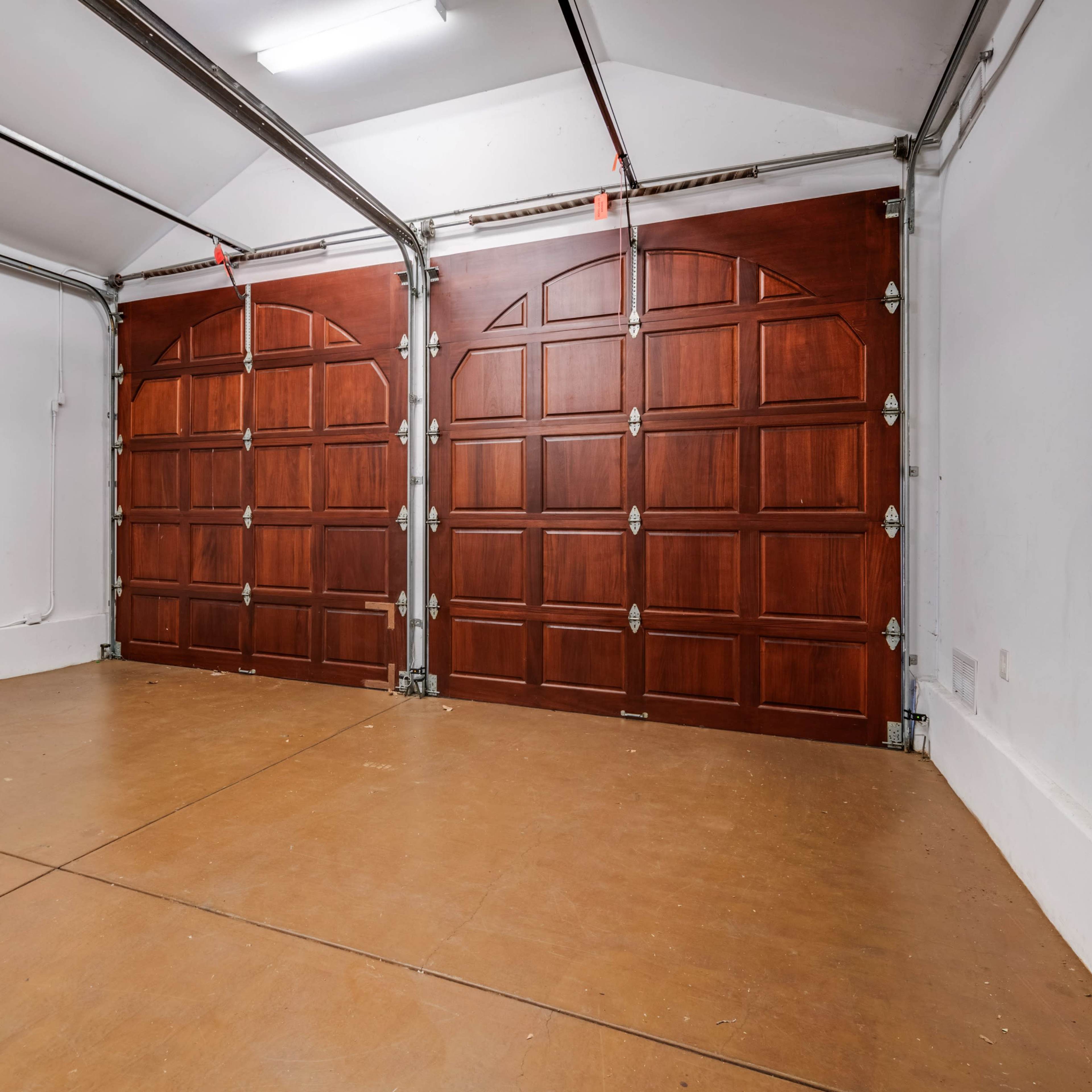 An empty garage with two wooden garage doors and a concrete floor.