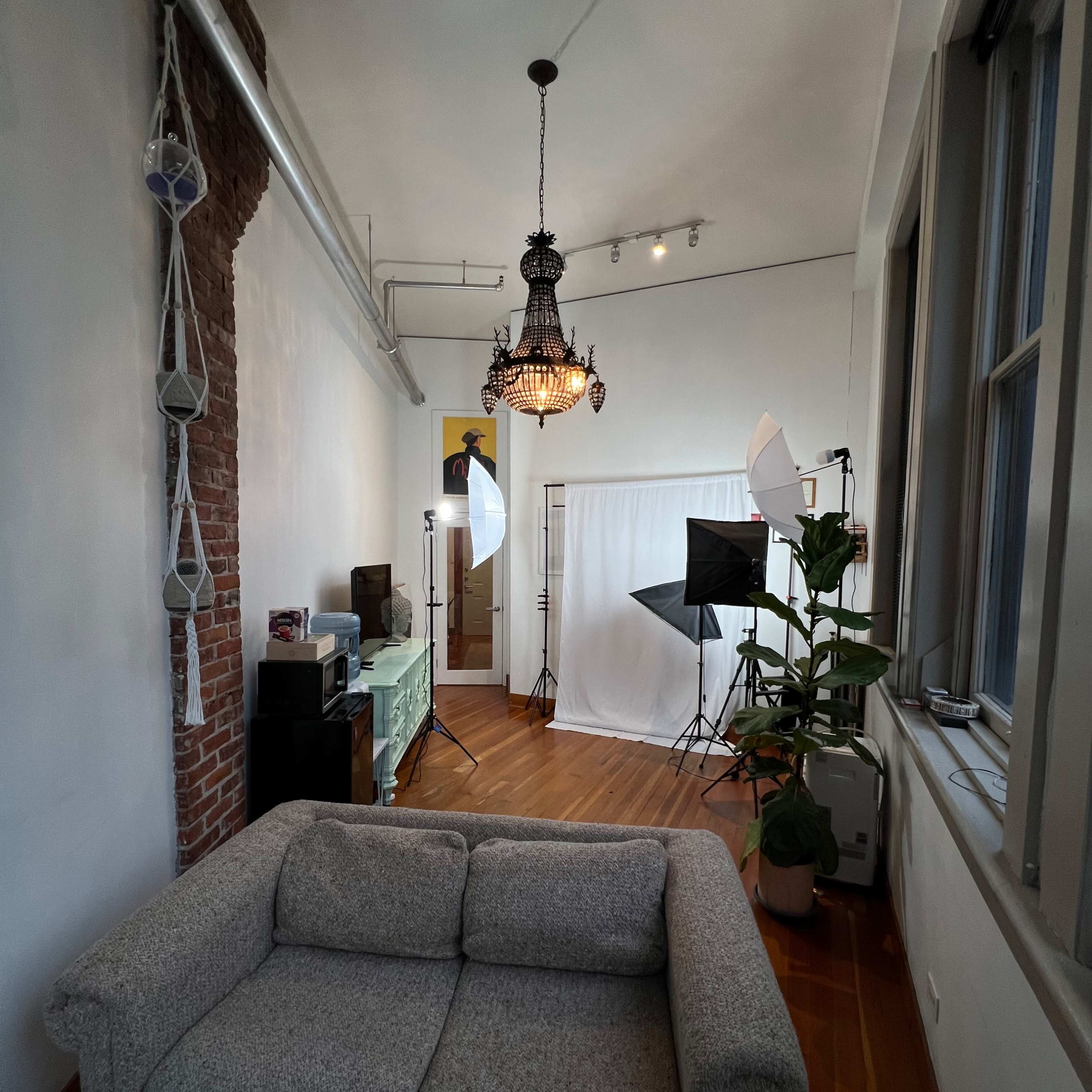 A bright room with a couch, a chandelier, and photography equipment set up against a backdrop.