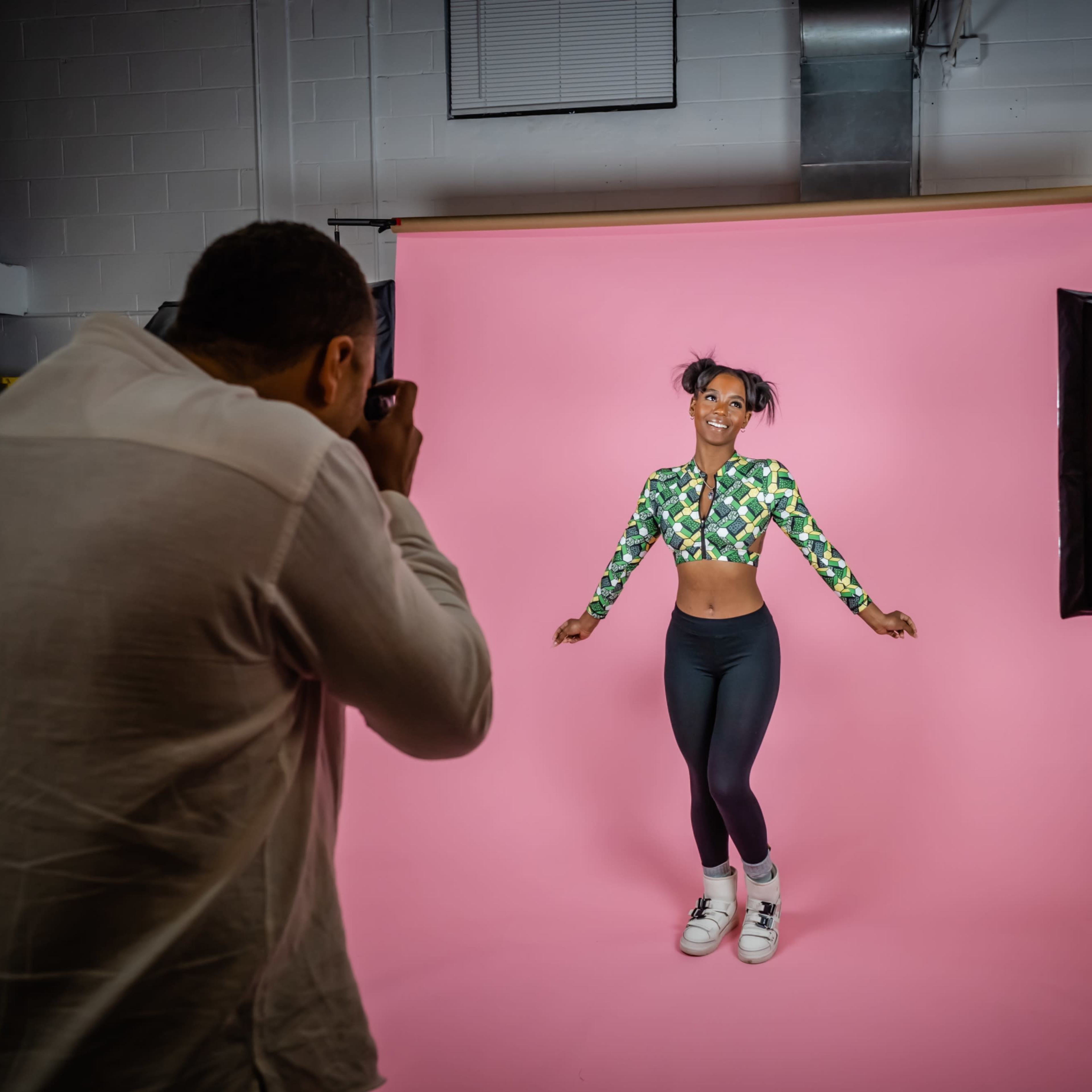 A photographer captures a model posing in front of a pink backdrop in a studio setting.