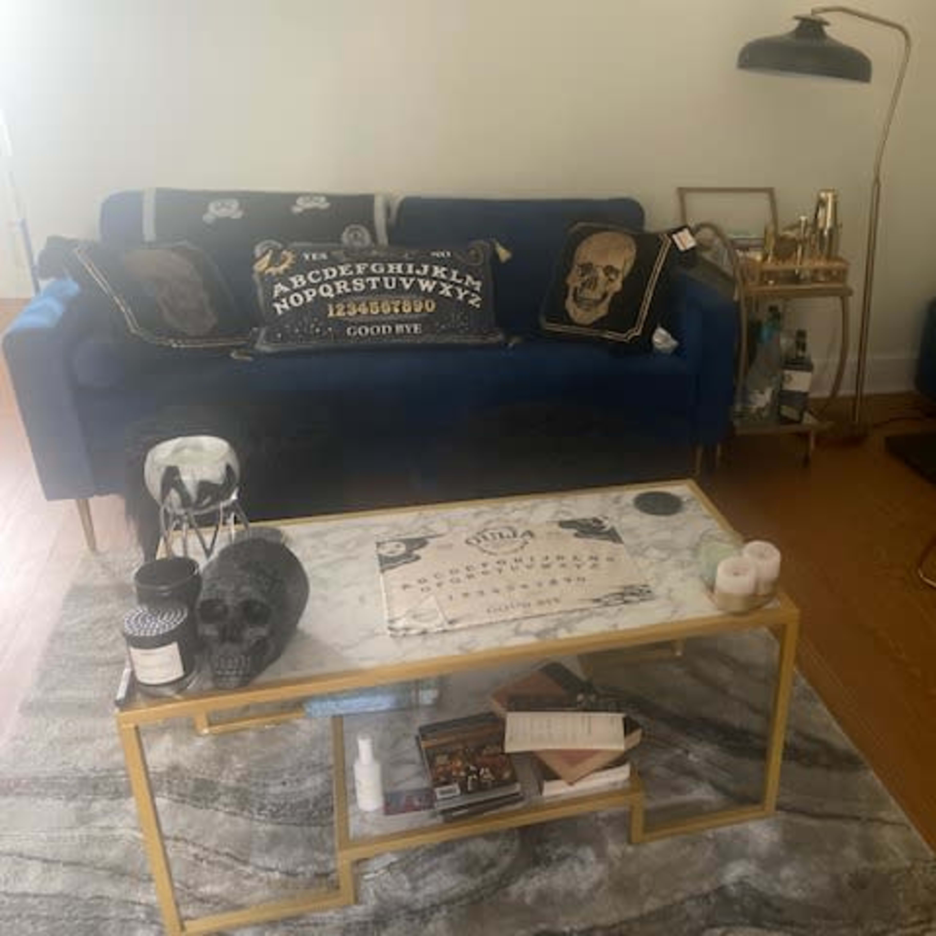 A living room with a blue sofa adorned with decorative pillows, a marble coffee table, and a small desk in the corner.