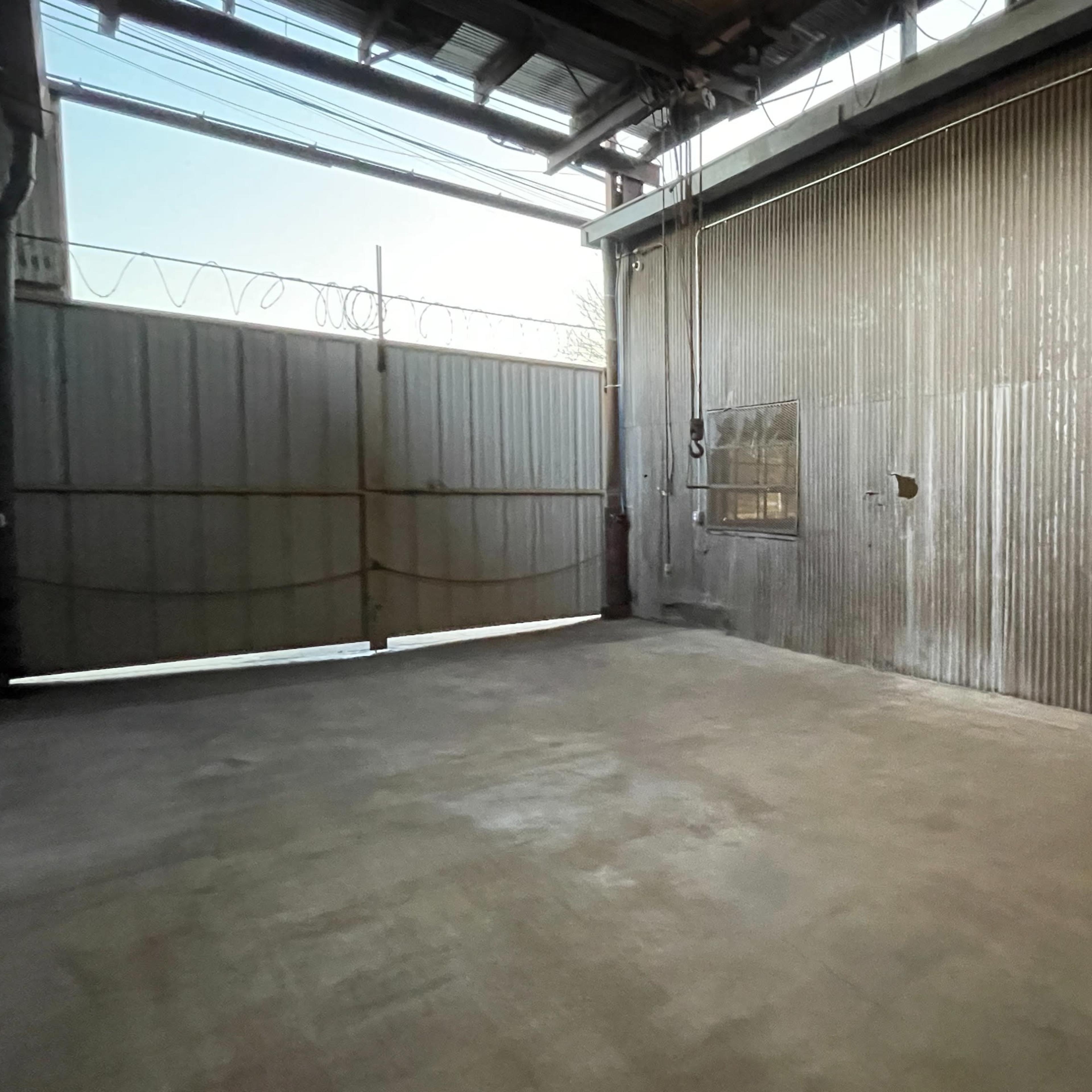 An empty industrial space with a corrugated metal wall and large open gates.