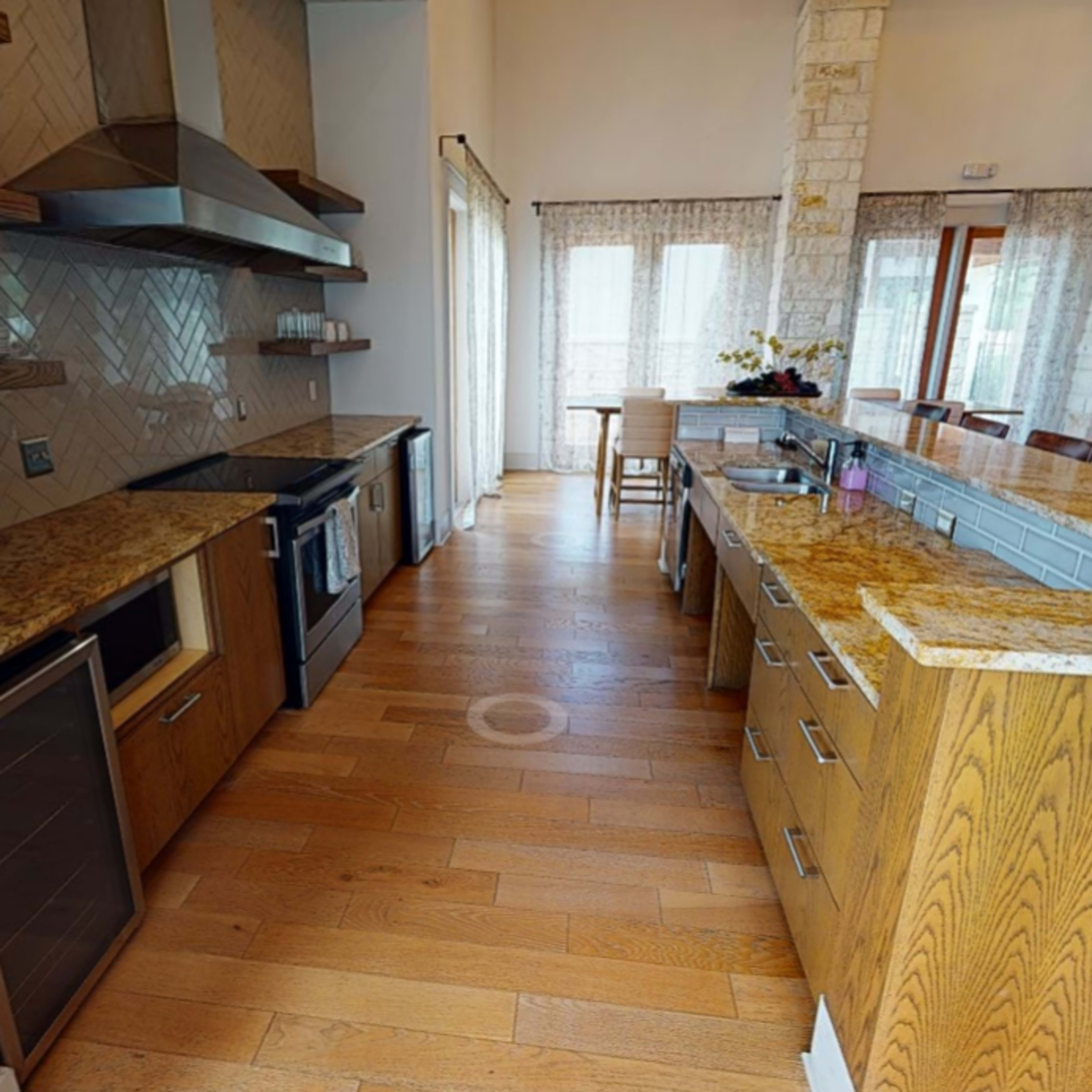 A modern kitchen with wooden cabinets, granite countertops, and large windows allowing natural light to enter.
