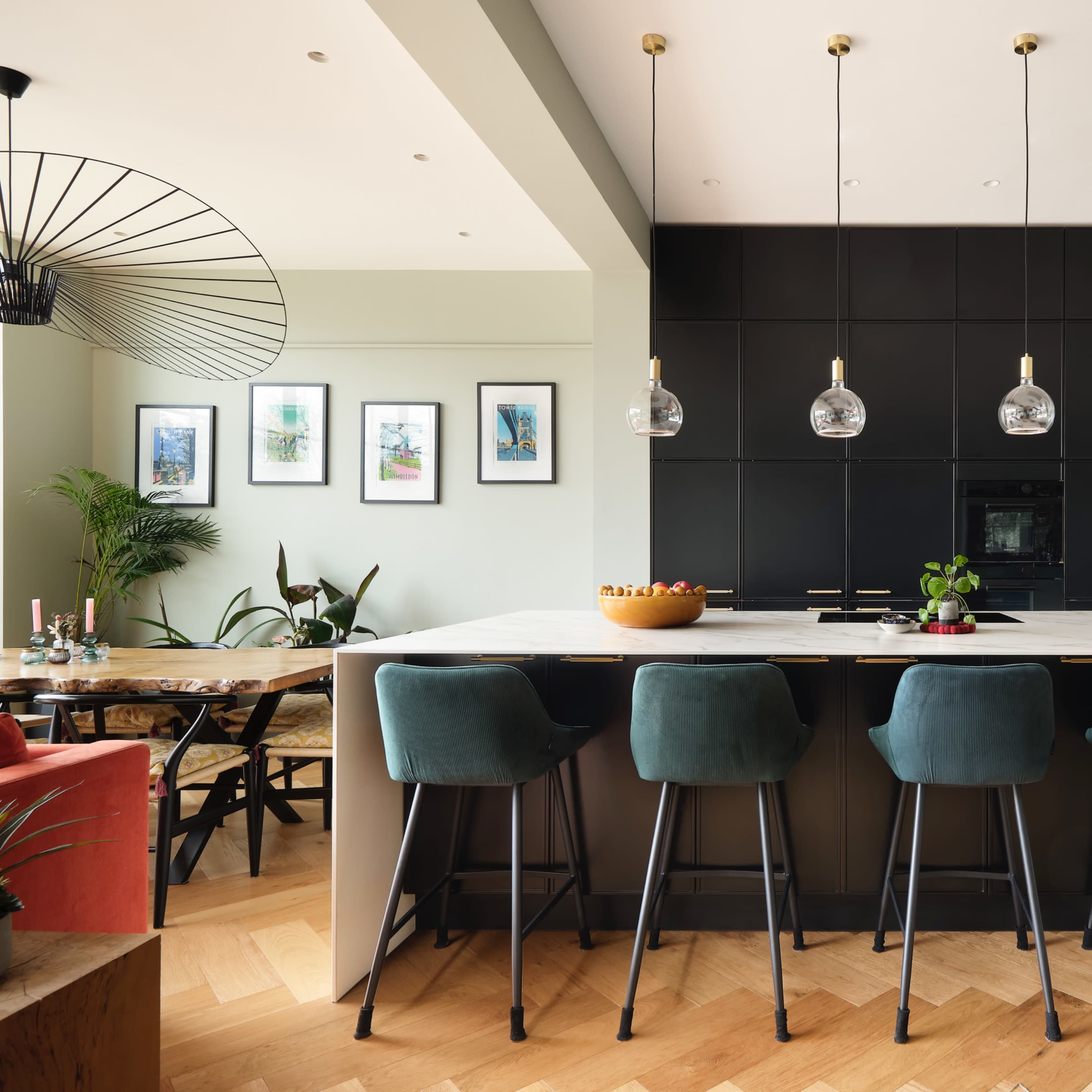 A modern kitchen features a central island with bar stools, dark cabinetry, and geometric lighting.