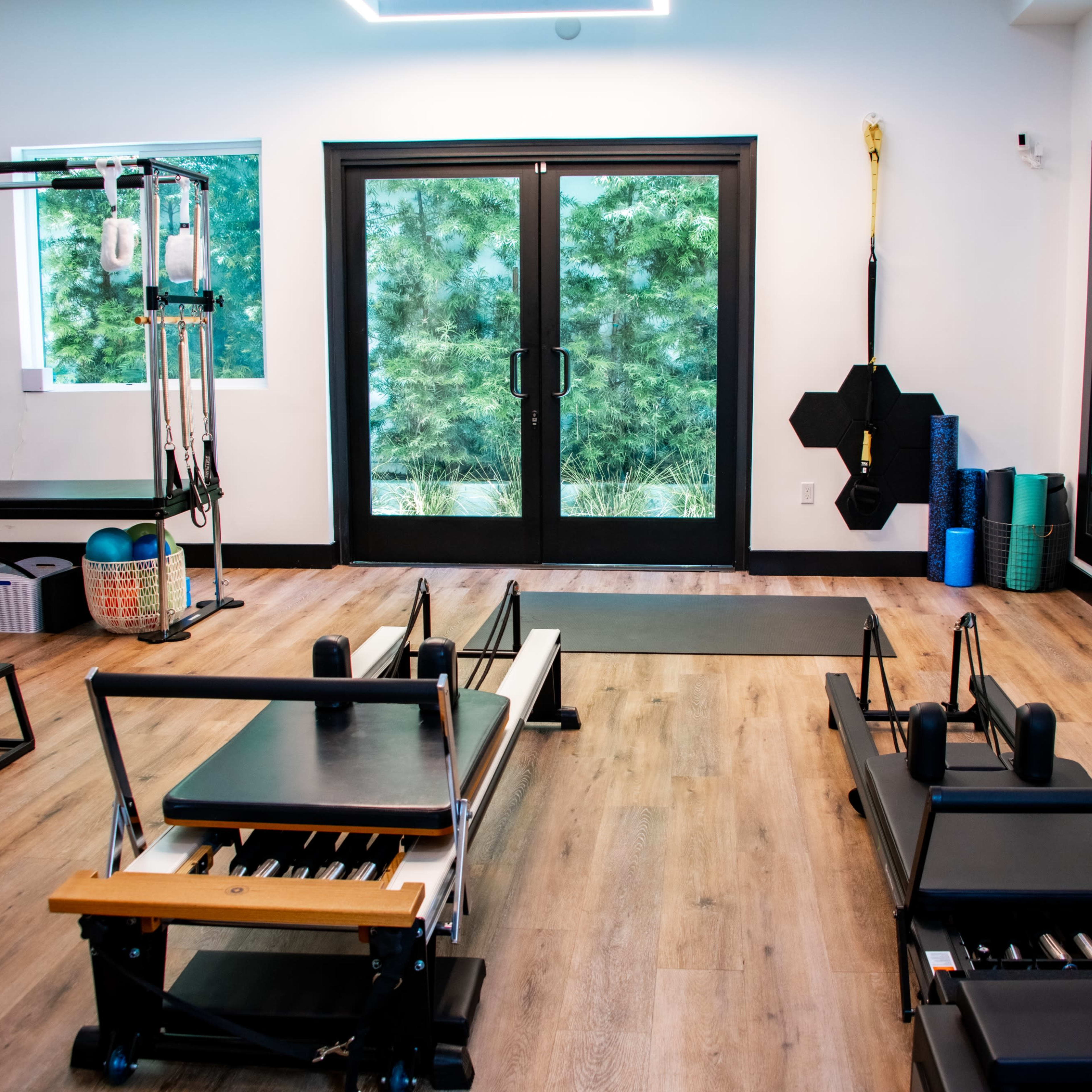 A modern Pilates studio with reformer machines, large windows, and exercise mats arranged against the walls.