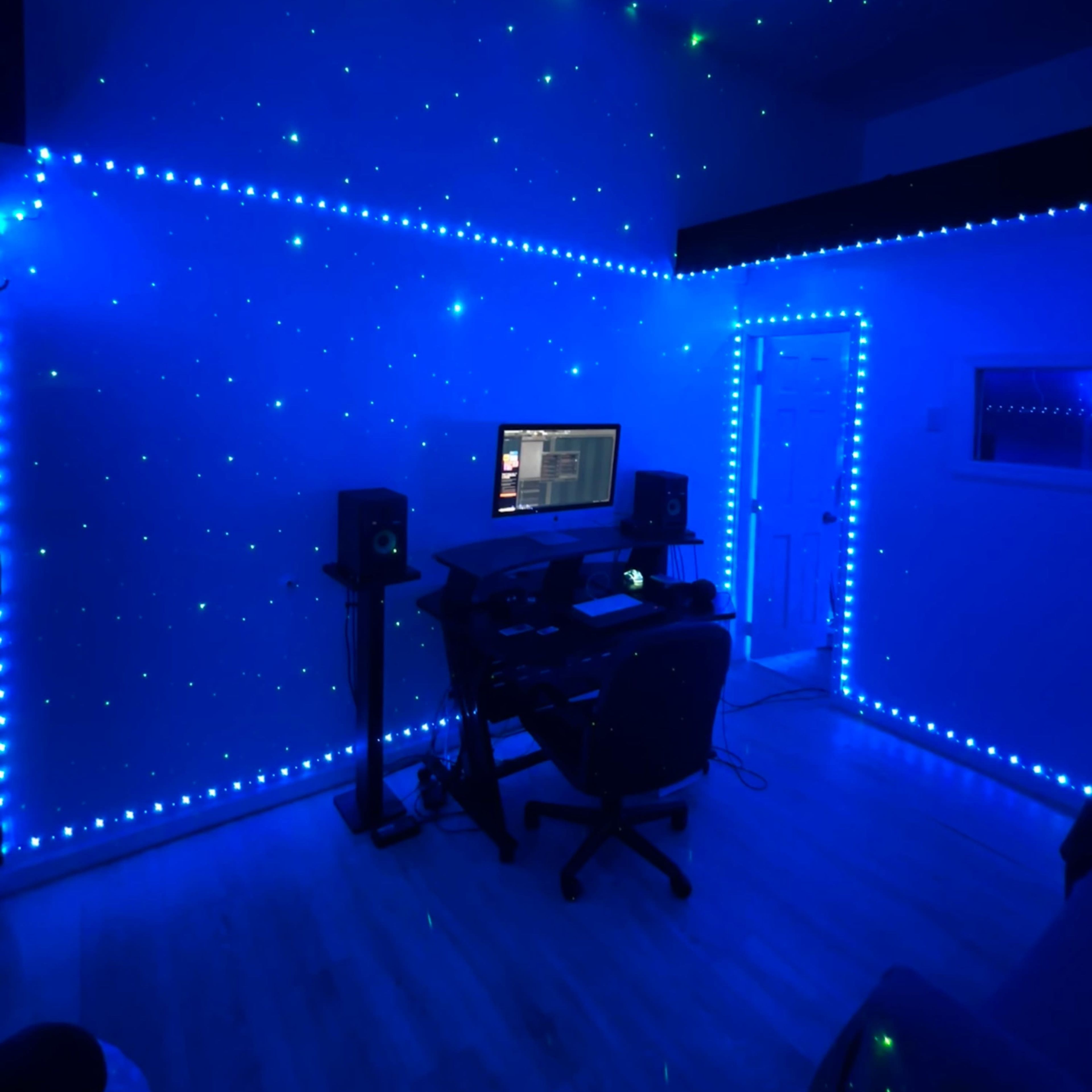 A dimly lit room with blue walls decorated with star-like lights, featuring a desk with a computer and audio speakers.