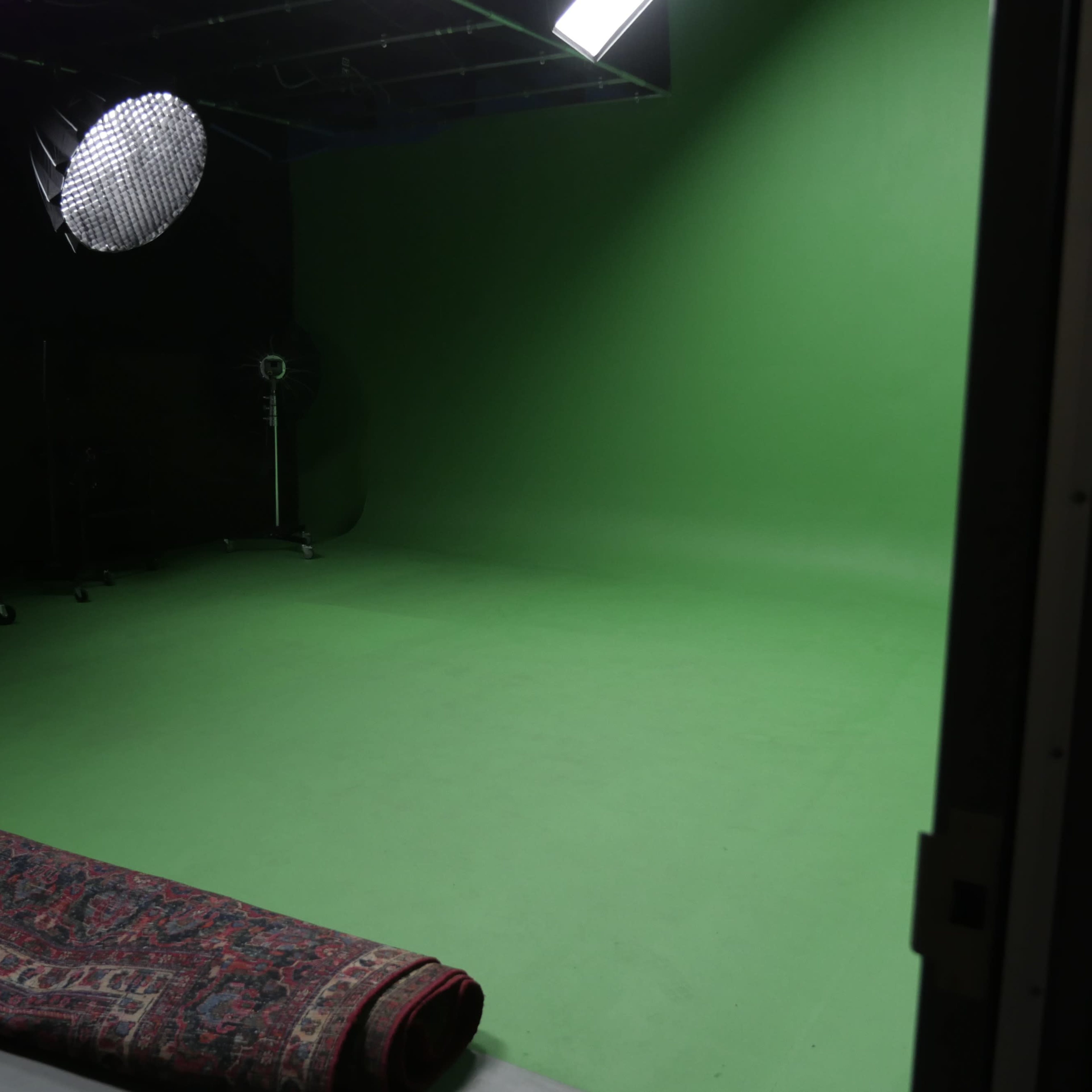 An empty green screen studio with a patterned rug rolled out on the floor.