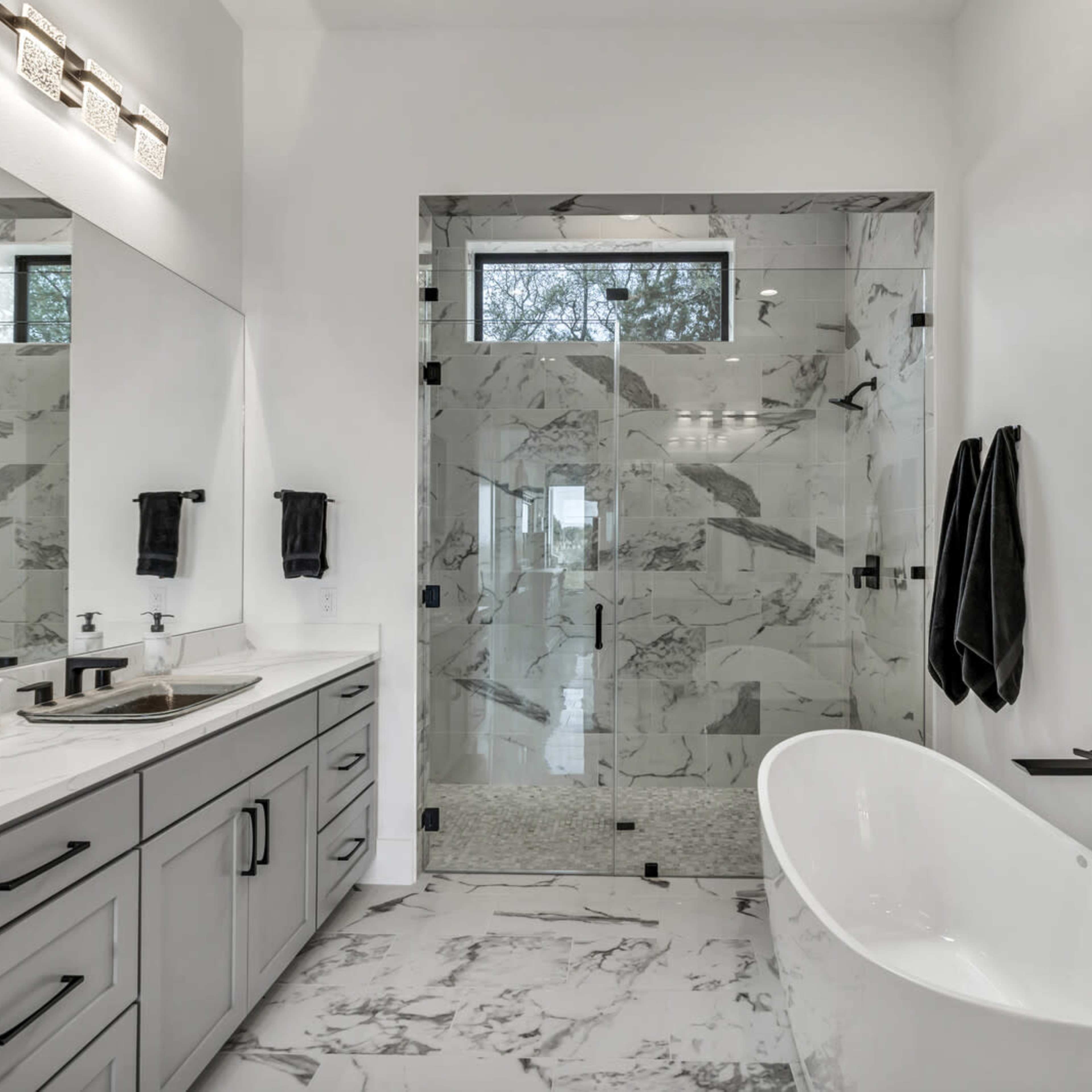 A modern bathroom featuring a glass shower enclosure, a freestanding tub, a double sink vanity, and marble-patterned tile flooring.