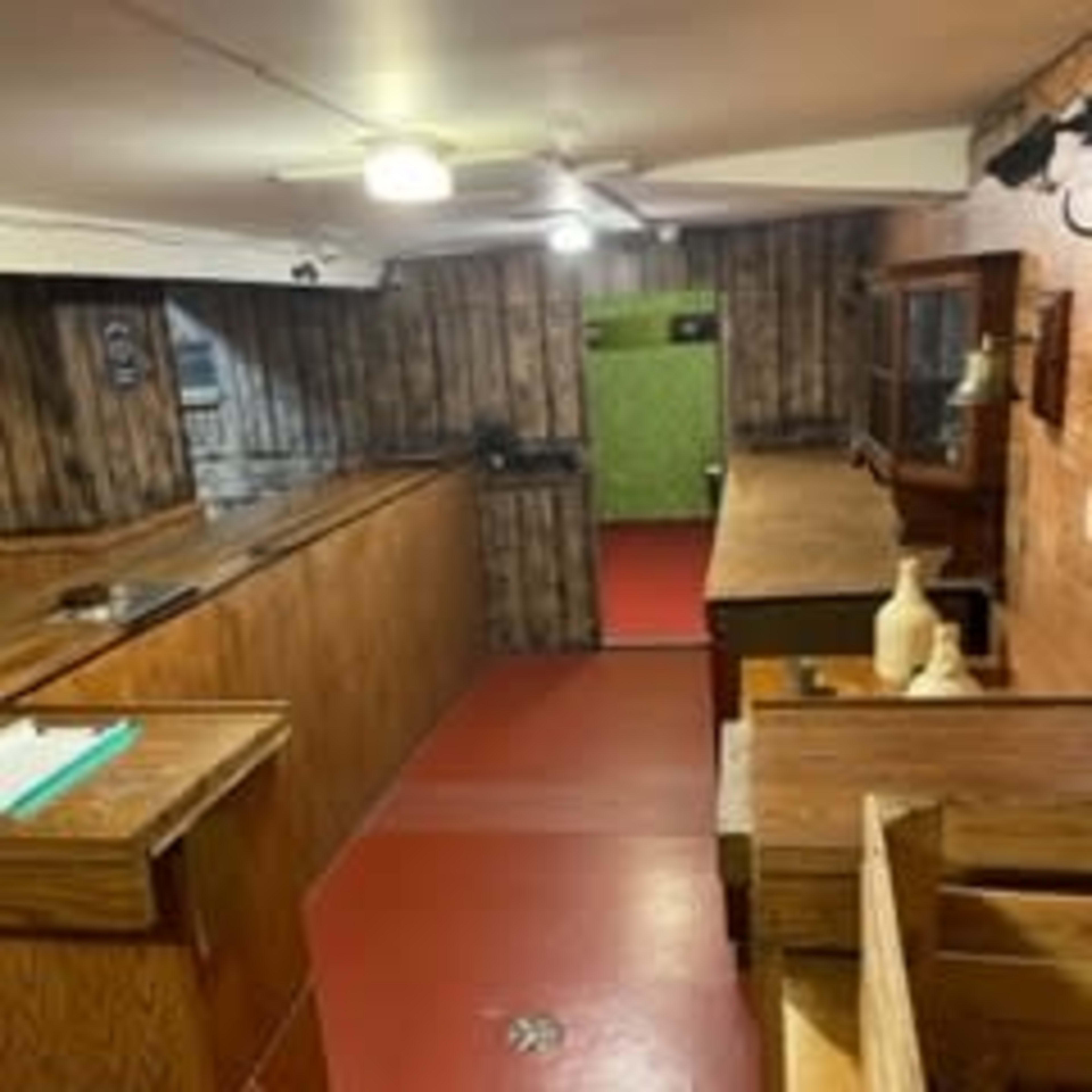 A basement kitchen with wooden cabinetry, a red floor, and a green wall at the far end.