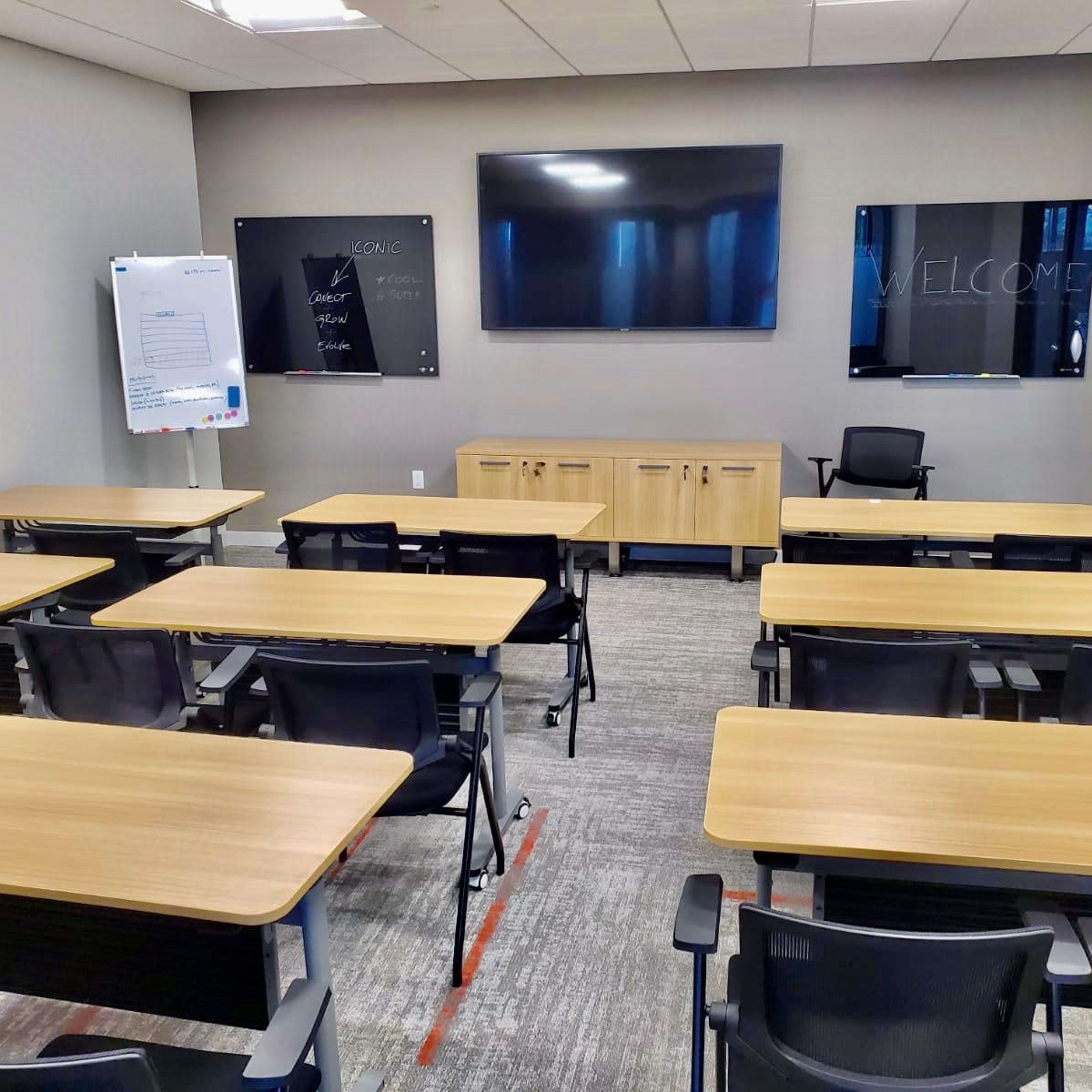 A modern classroom equipped with desks, chairs, and two large screens on the walls.