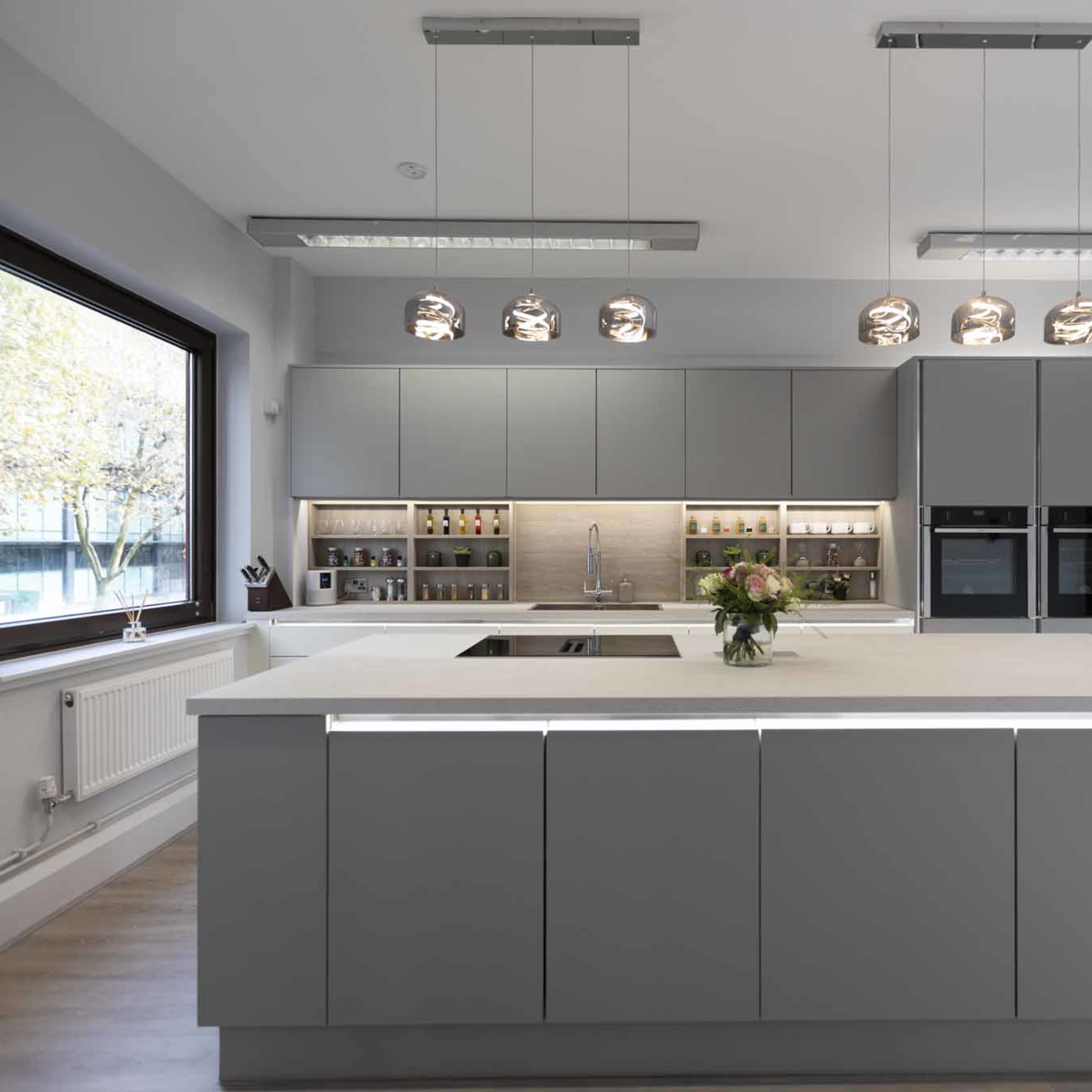 A modern kitchen with a large central island, gray cabinetry, and pendant lighting above.