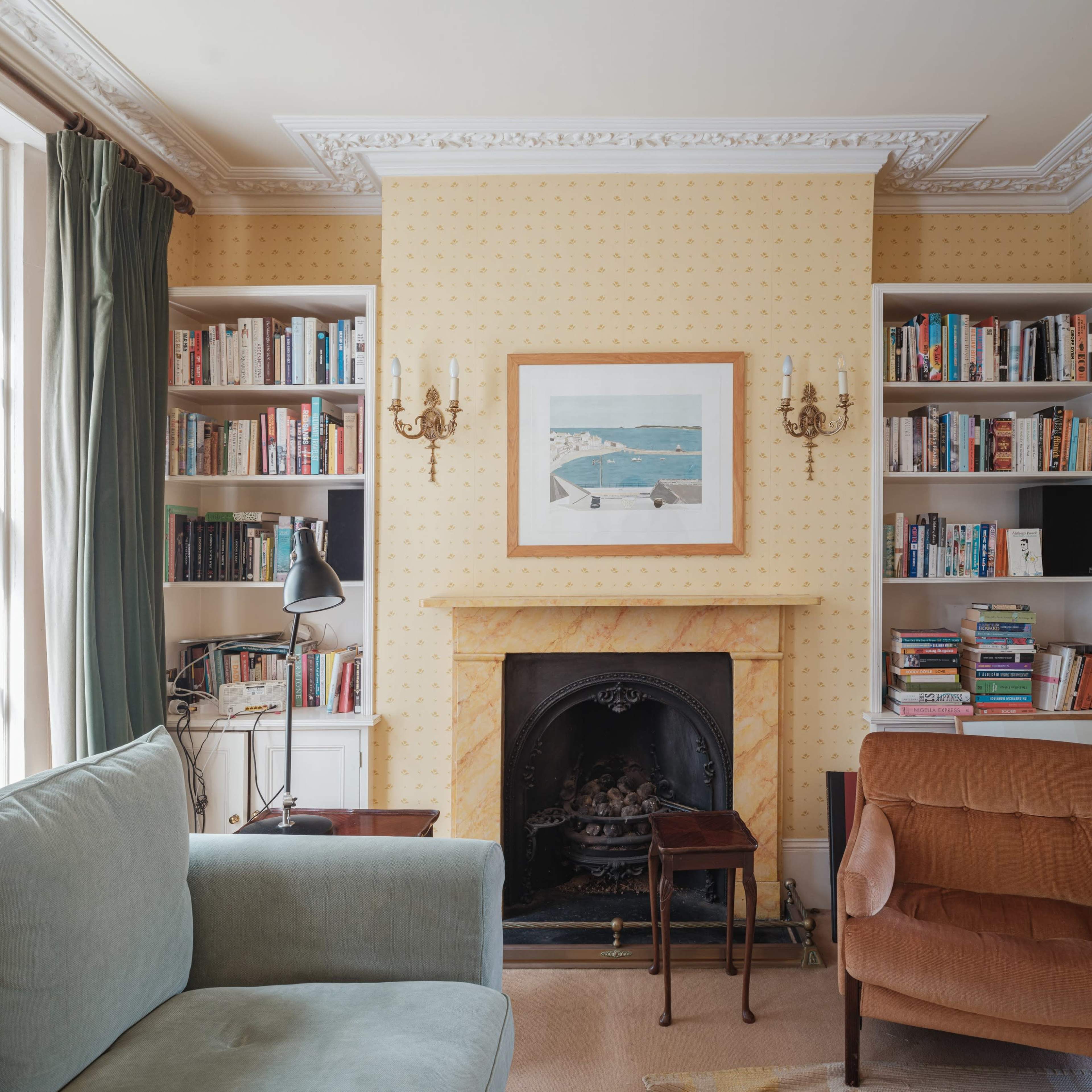 A cozy living room features a fireplace surrounded by bookshelves, a framed painting on the wall, and a sofa paired with an armchair.