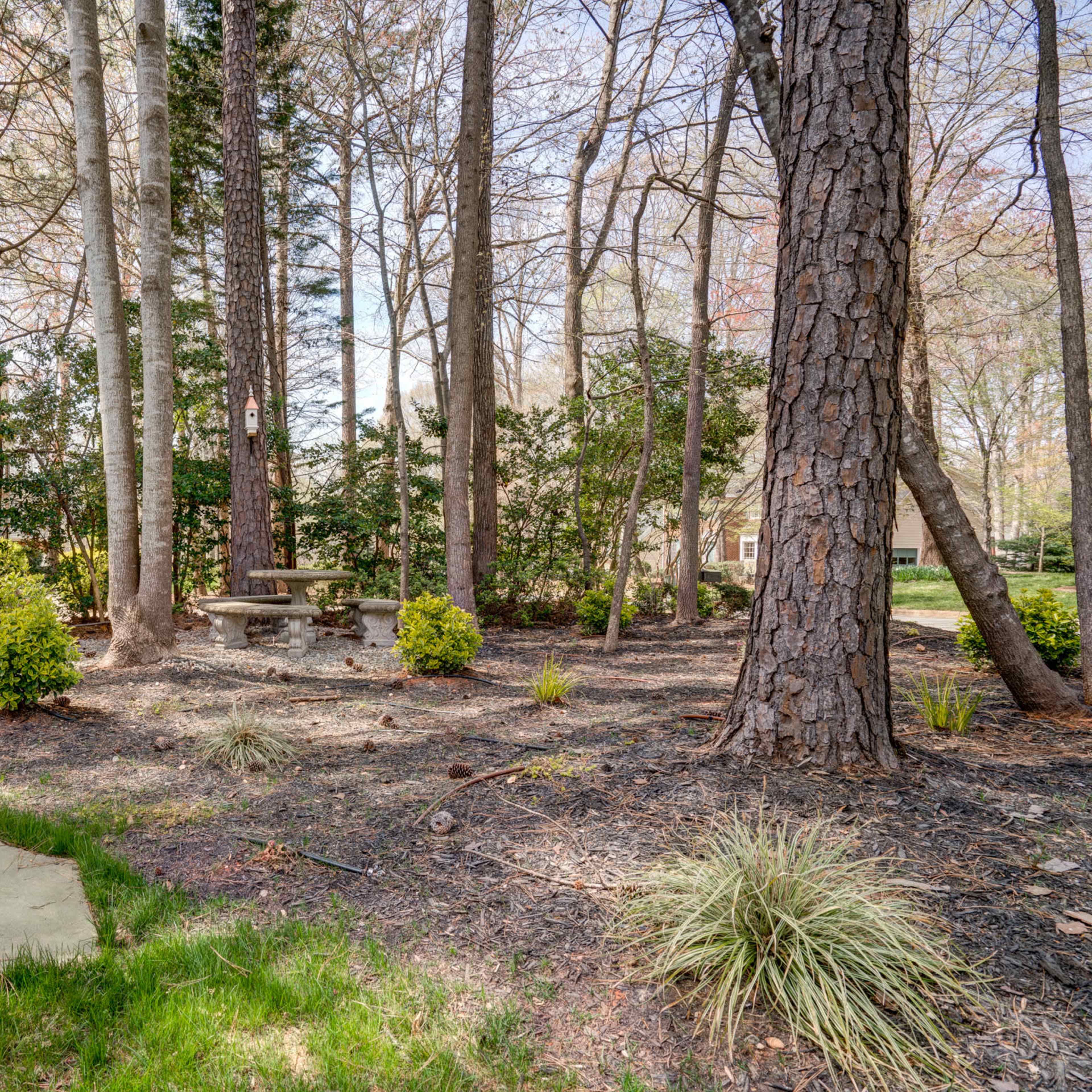 A stone table and bench are surrounded by grass and trees in a landscaped garden area.