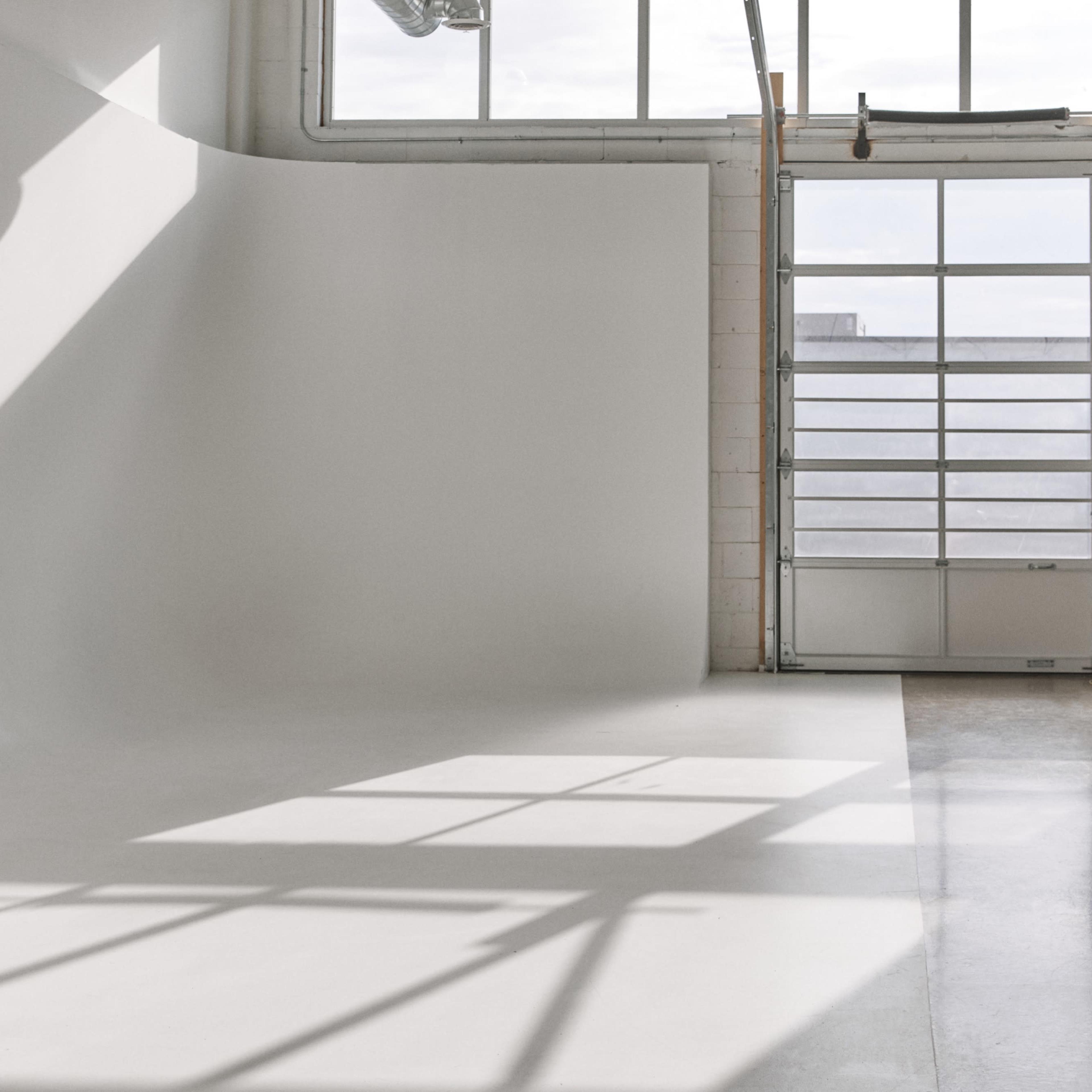 A bright studio space with a curved white wall and large windows casting shadows on the floor.