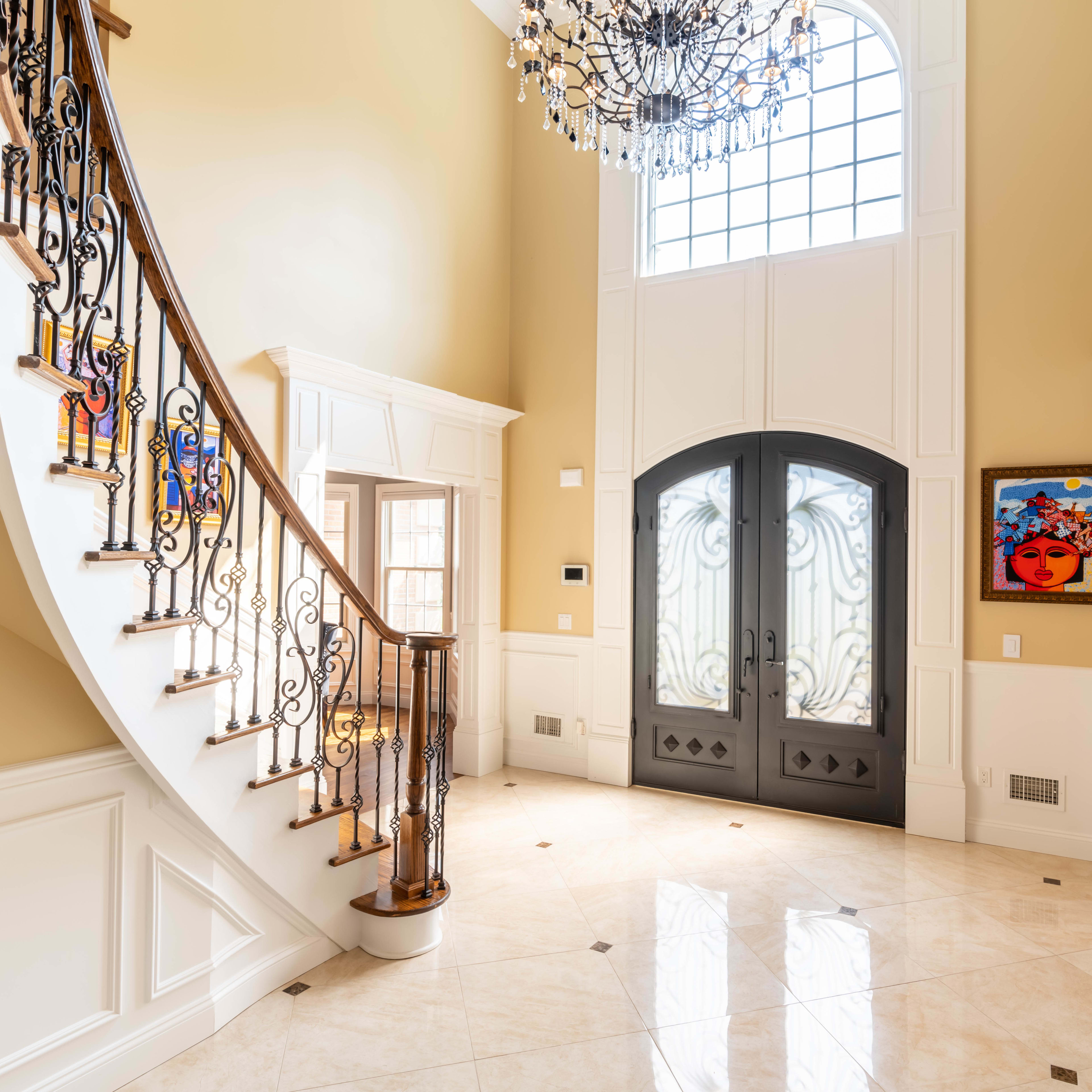 A grand foyer features a curved staircase, ornate chandelier, and double front doors with decorative glass panels.