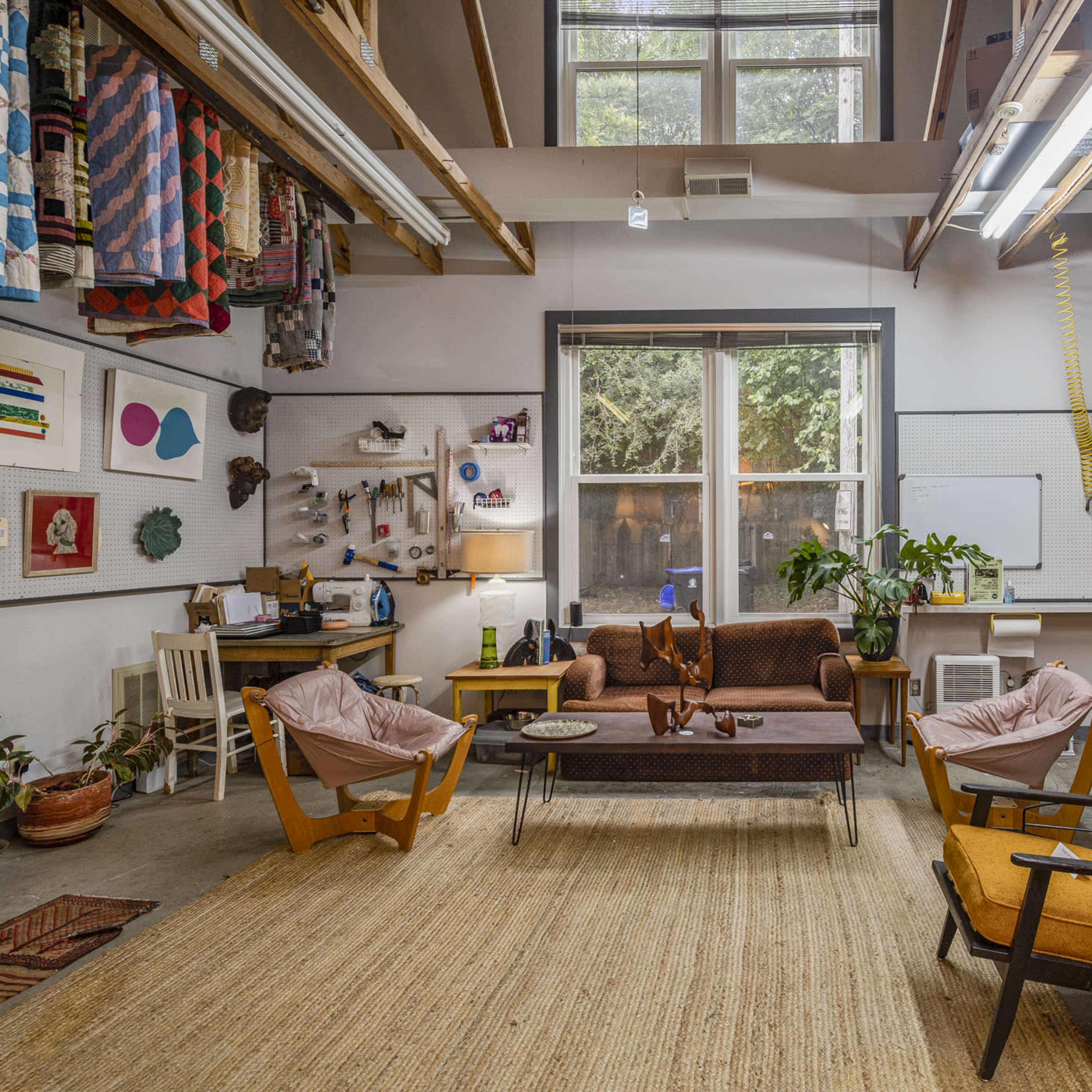 A spacious indoor area with wooden beams, featuring a mix of seating options, decorative textiles on the walls, and large windows allowing natural light.