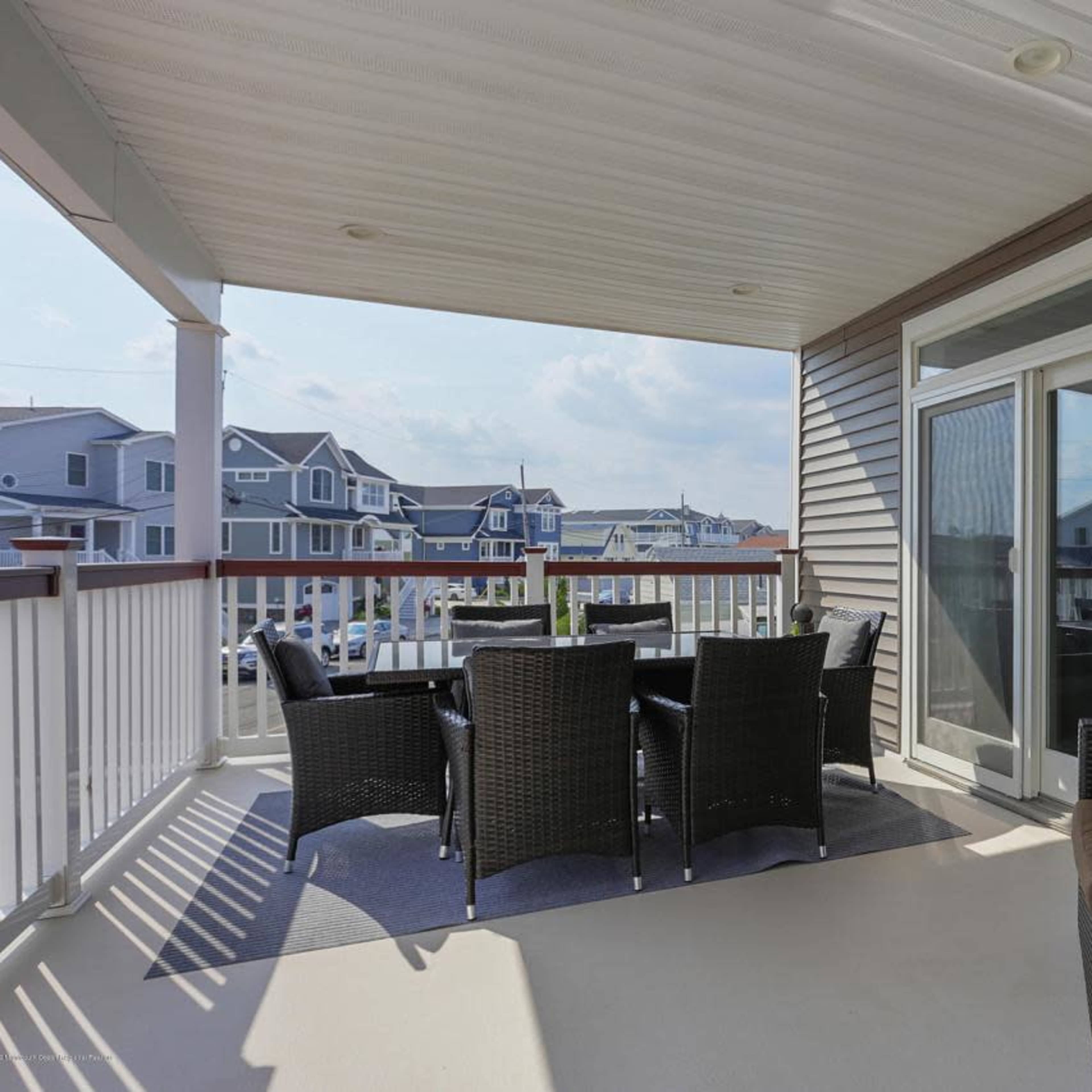 A spacious balcony with a dining table and chairs, surrounded by a railing and overlooking nearby houses.