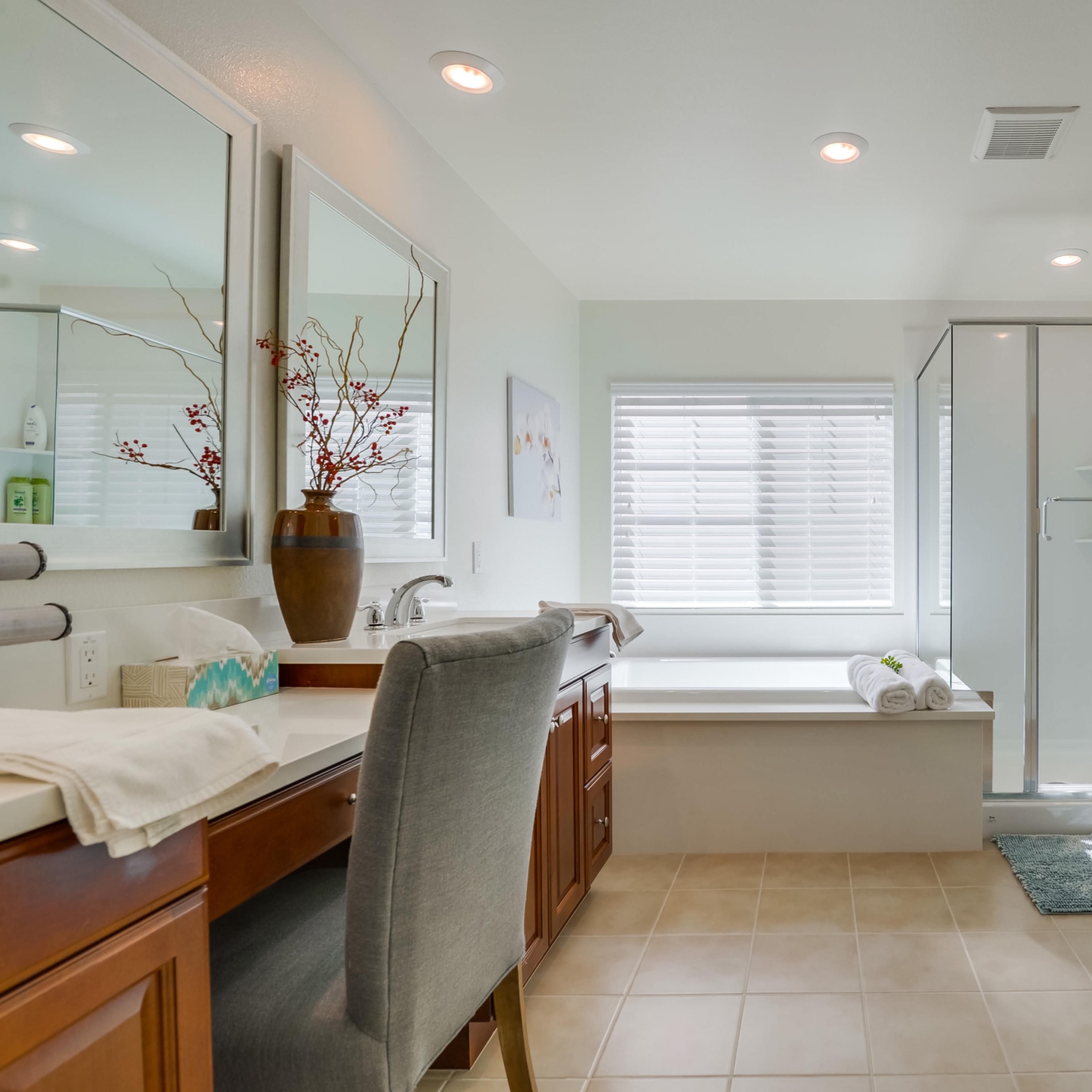 A well-lit bathroom featuring a vanity with a chair, a clawfoot bathtub, and a separate glass-enclosed shower.