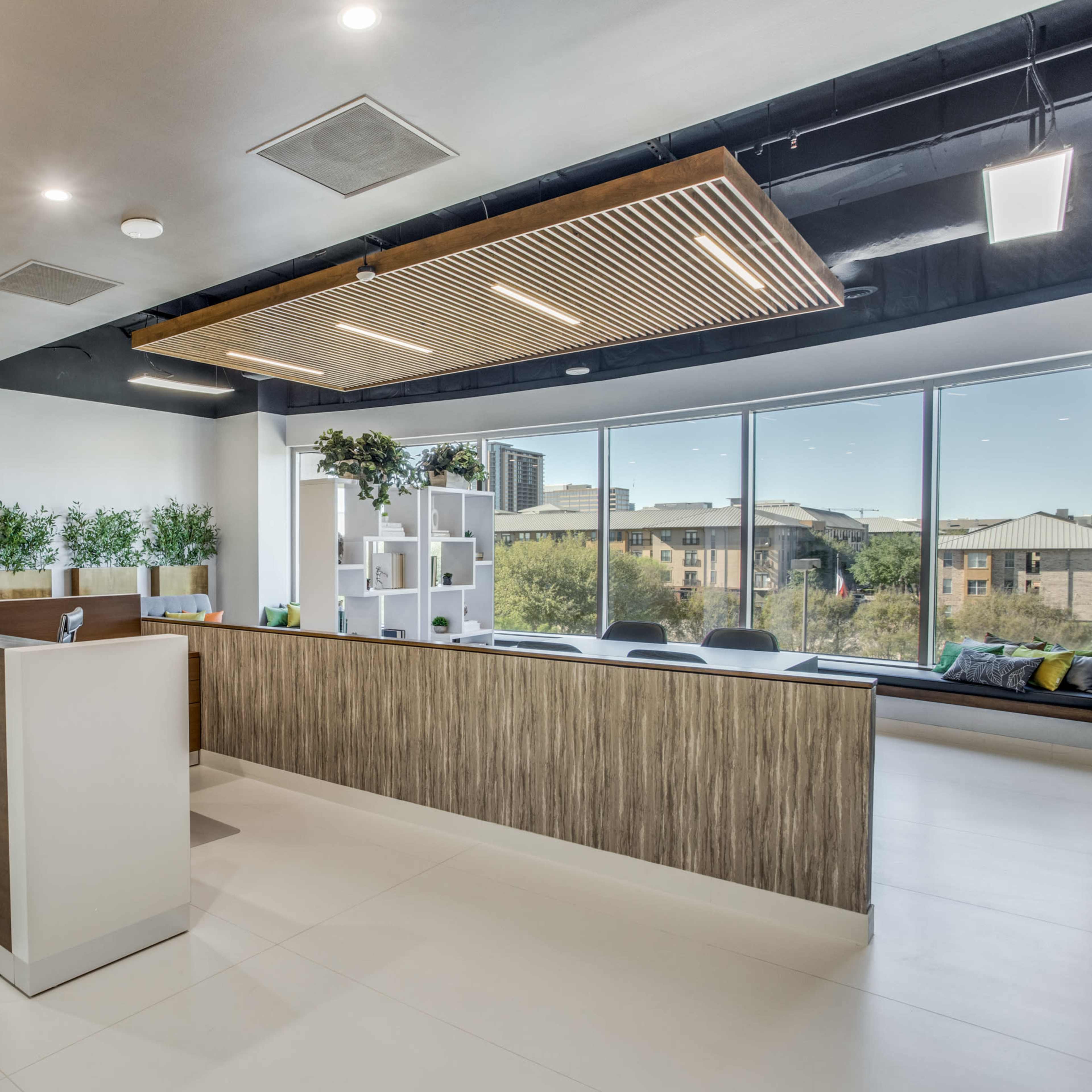 A modern reception area with a wooden front desk and large windows offering a view of an outdoor landscape.