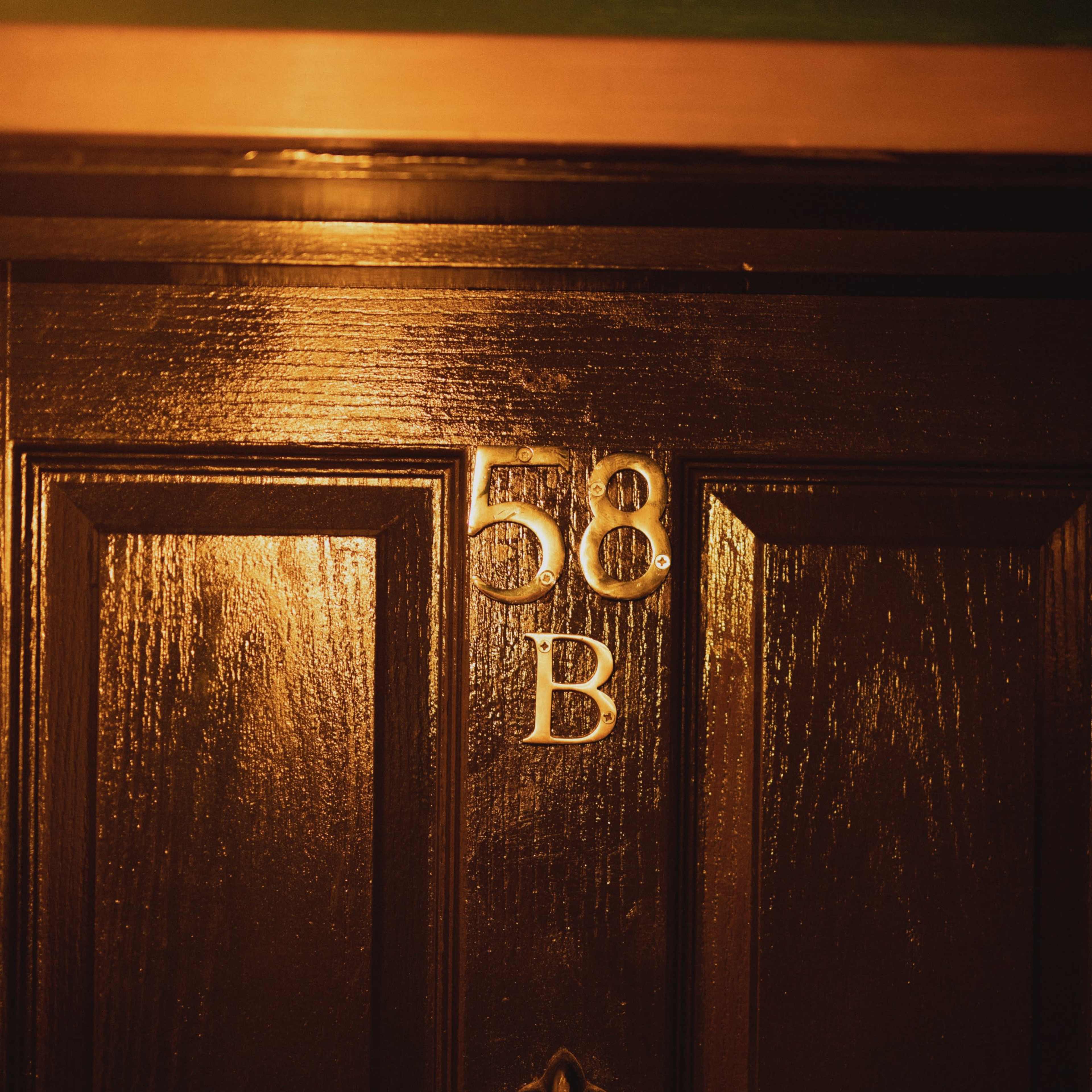 A dark wooden door with the number "58" and the letter "B" displayed prominently above a circular door knocker.
