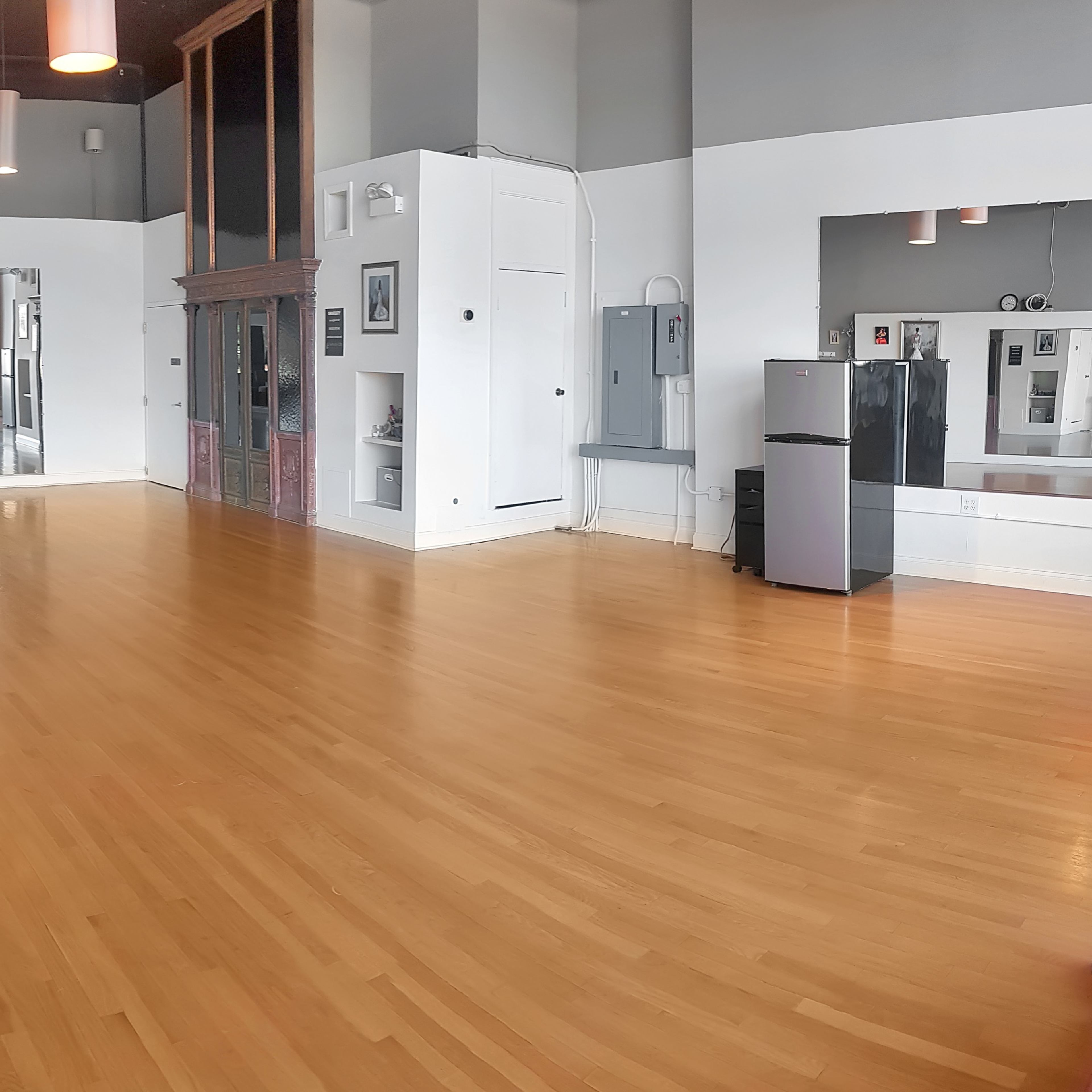 A spacious, empty dance studio with wooden flooring, large mirrors on one wall, and minimal furnishings.