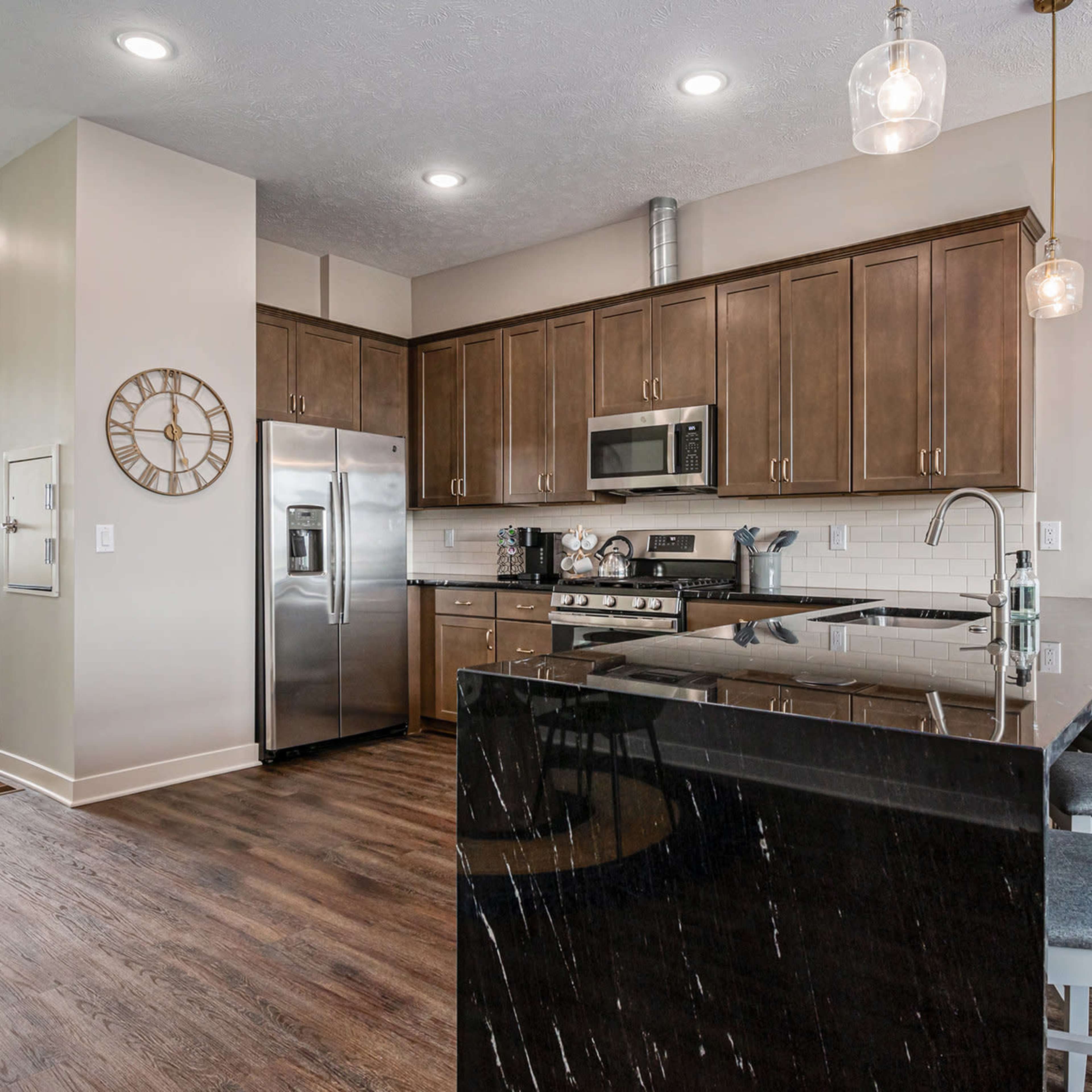 A modern kitchen features dark wood cabinetry, stainless steel appliances, and a large island with bar seating.