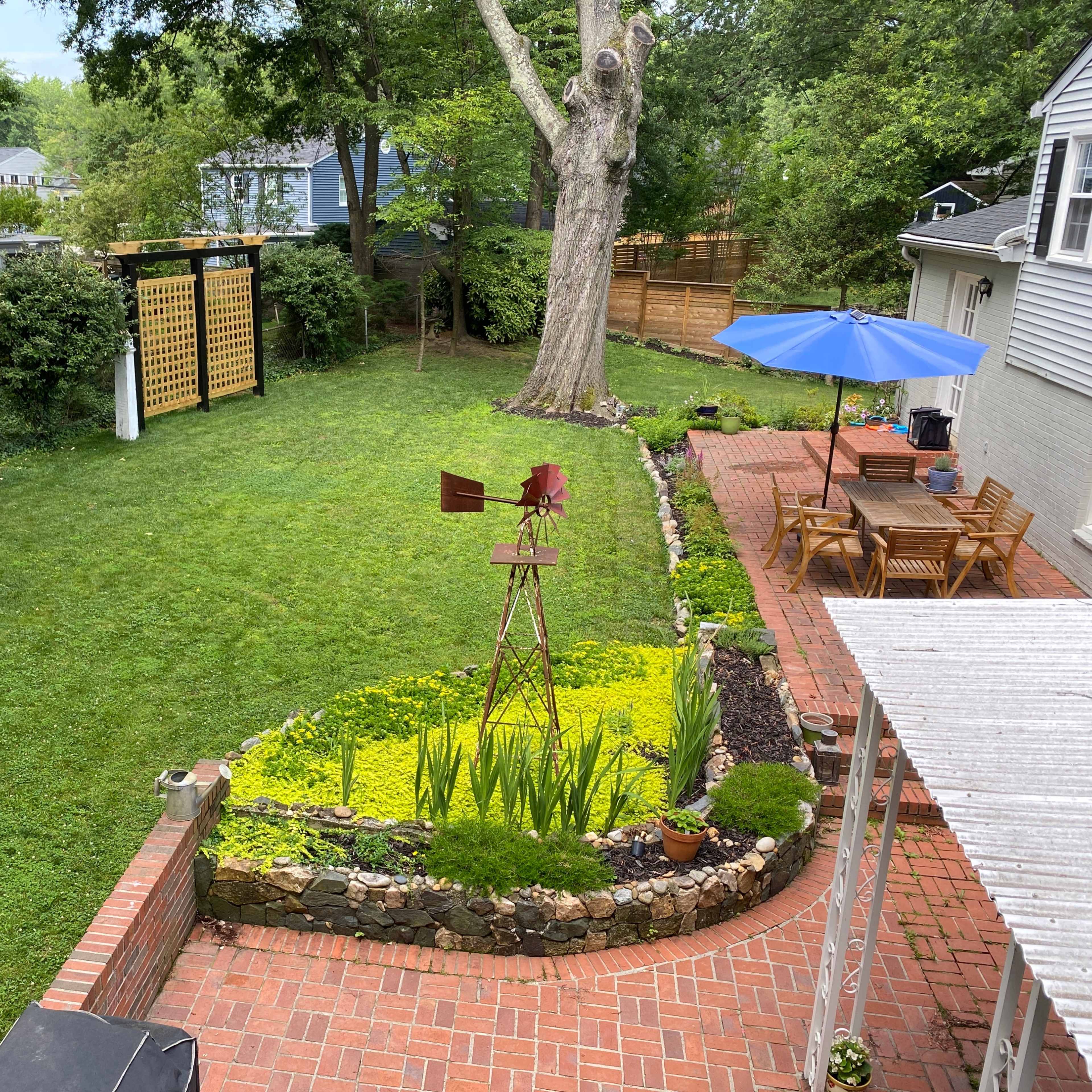 A landscaped backyard with a green lawn, stone borders, a gazebo, and wooden trellises on either side.