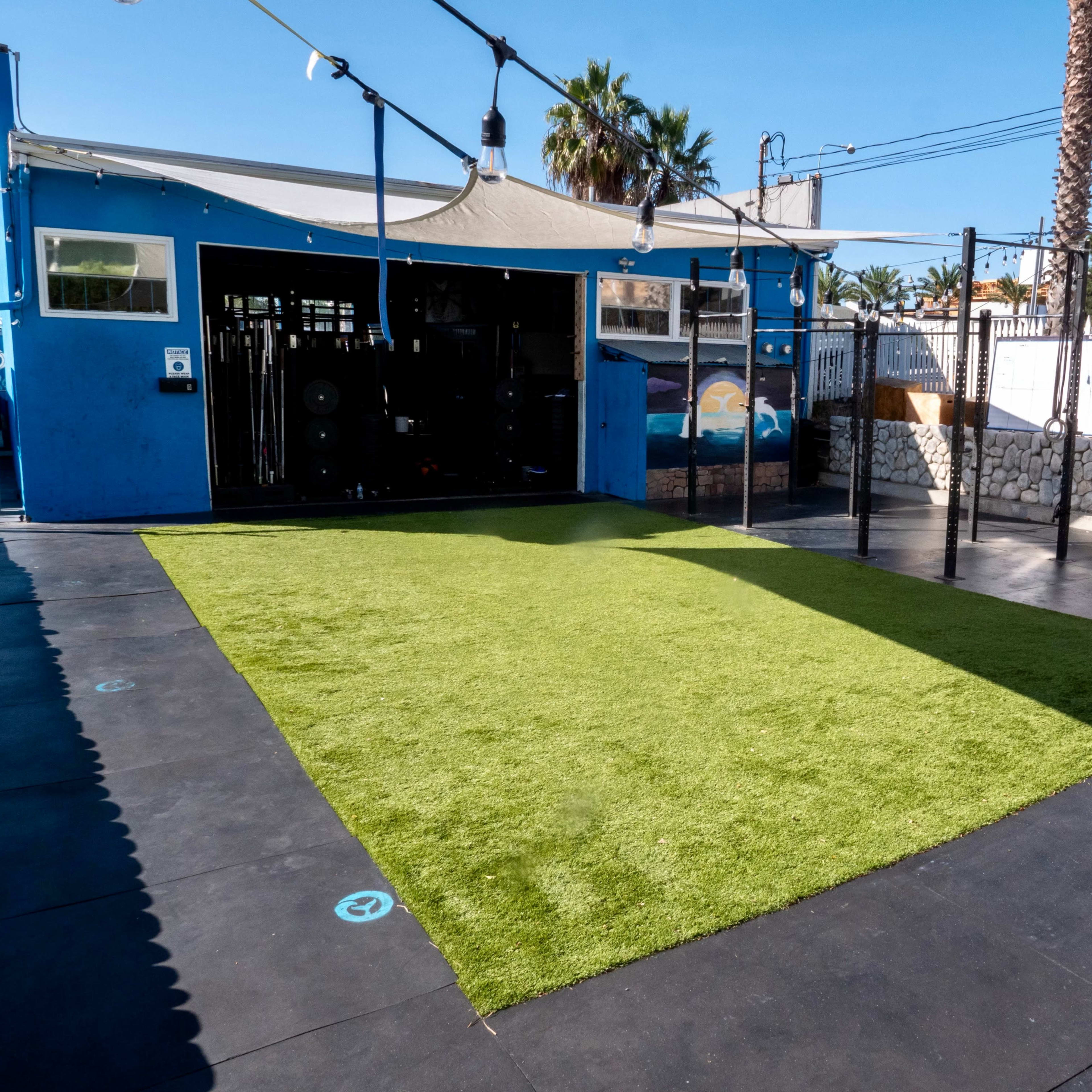A grassy area bordered by exercise equipment and a blue building with a patio.