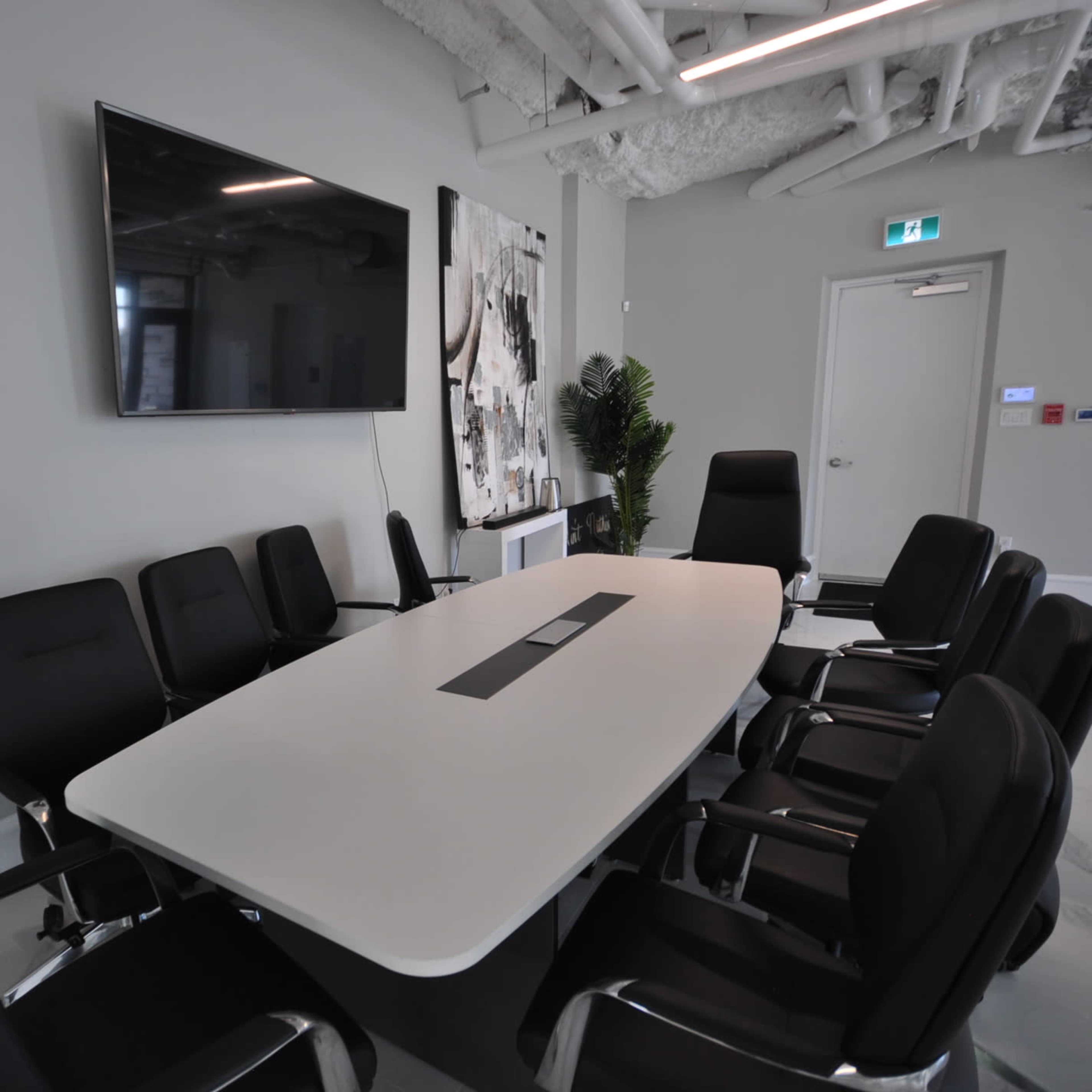 A modern conference room features a long white table surrounded by black chairs and a large wall-mounted television.