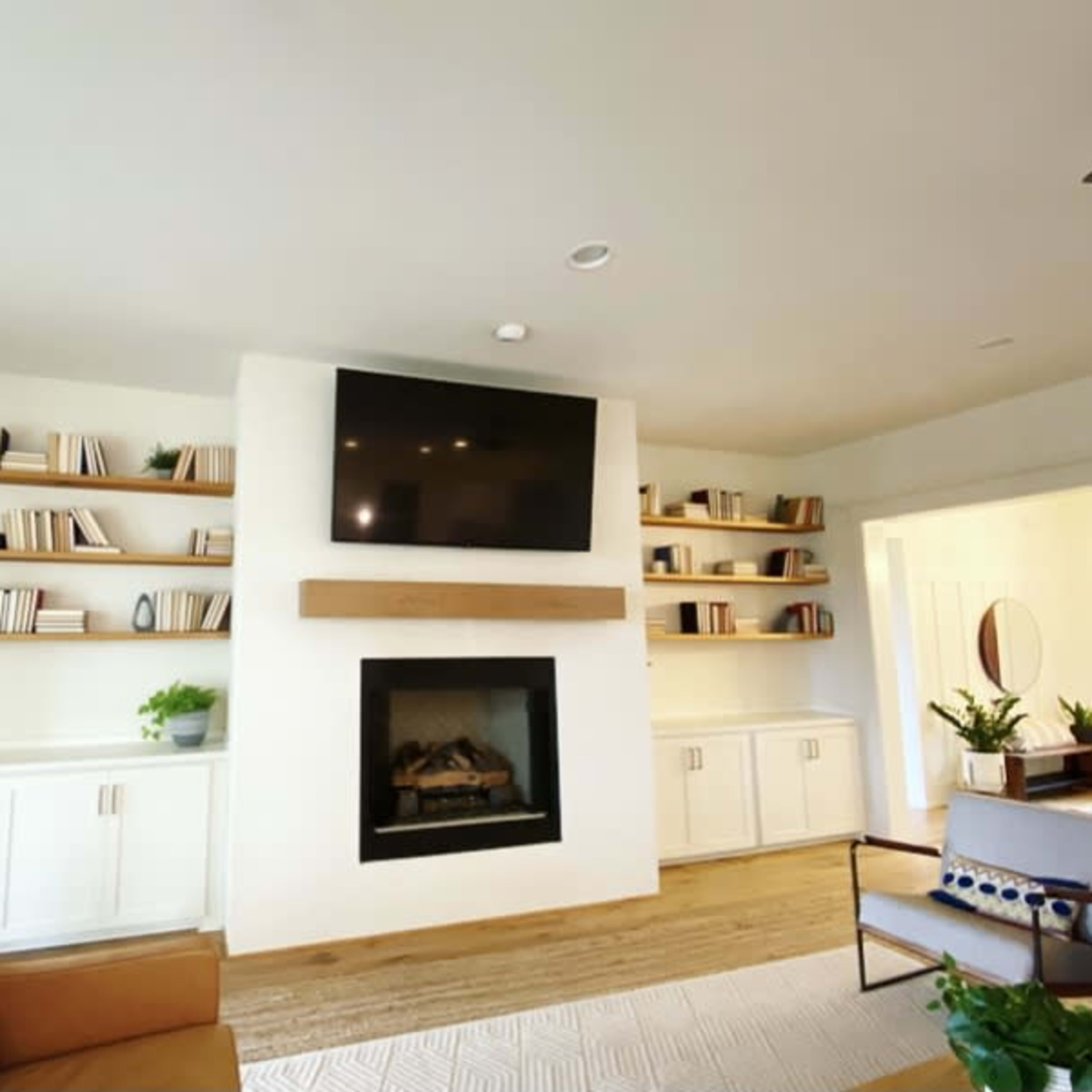 A living room features a fireplace with a television mounted above it and built-in shelves filled with books on either side.