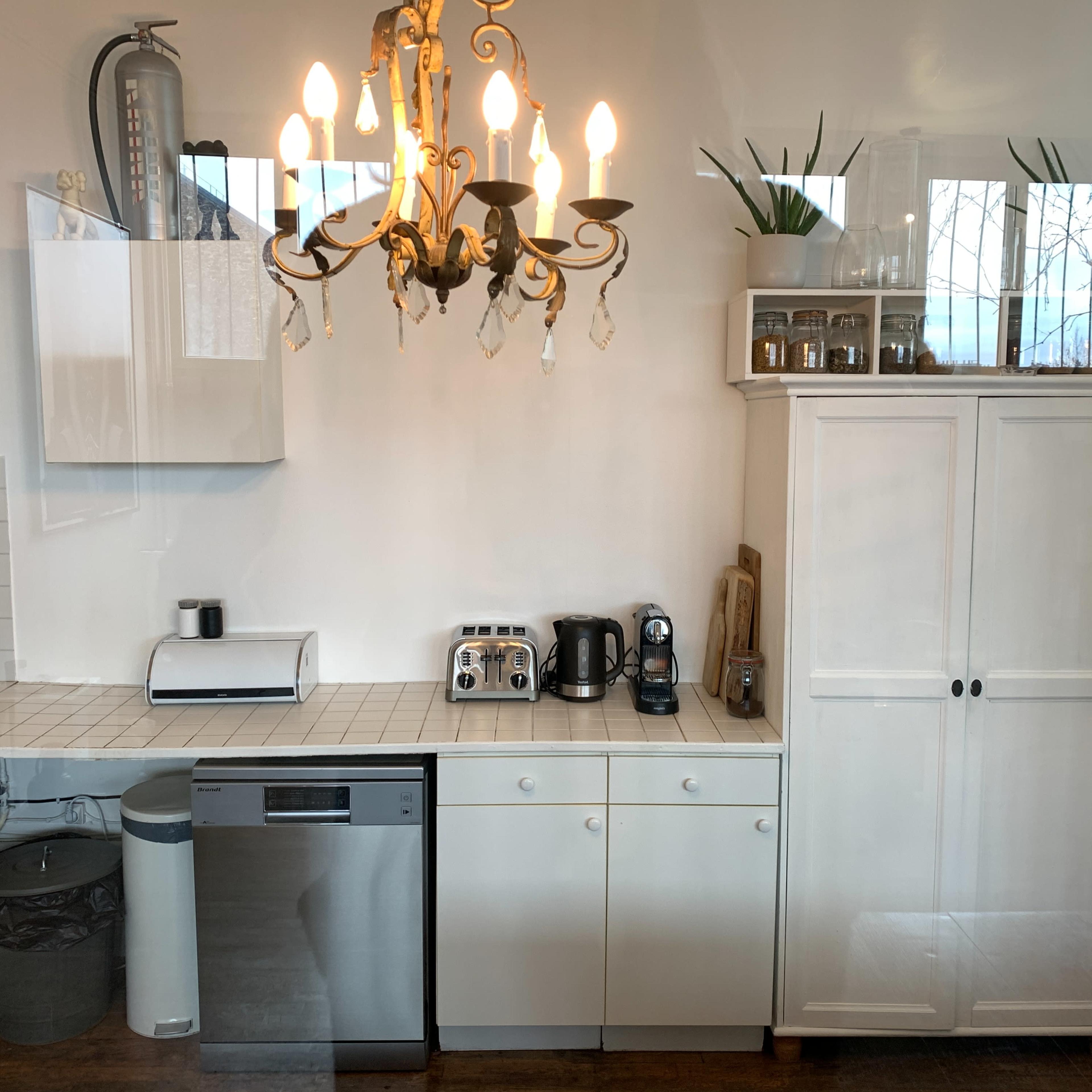 A tidy kitchen with white cabinetry, a chandelier, and various appliances arranged on the countertops.
