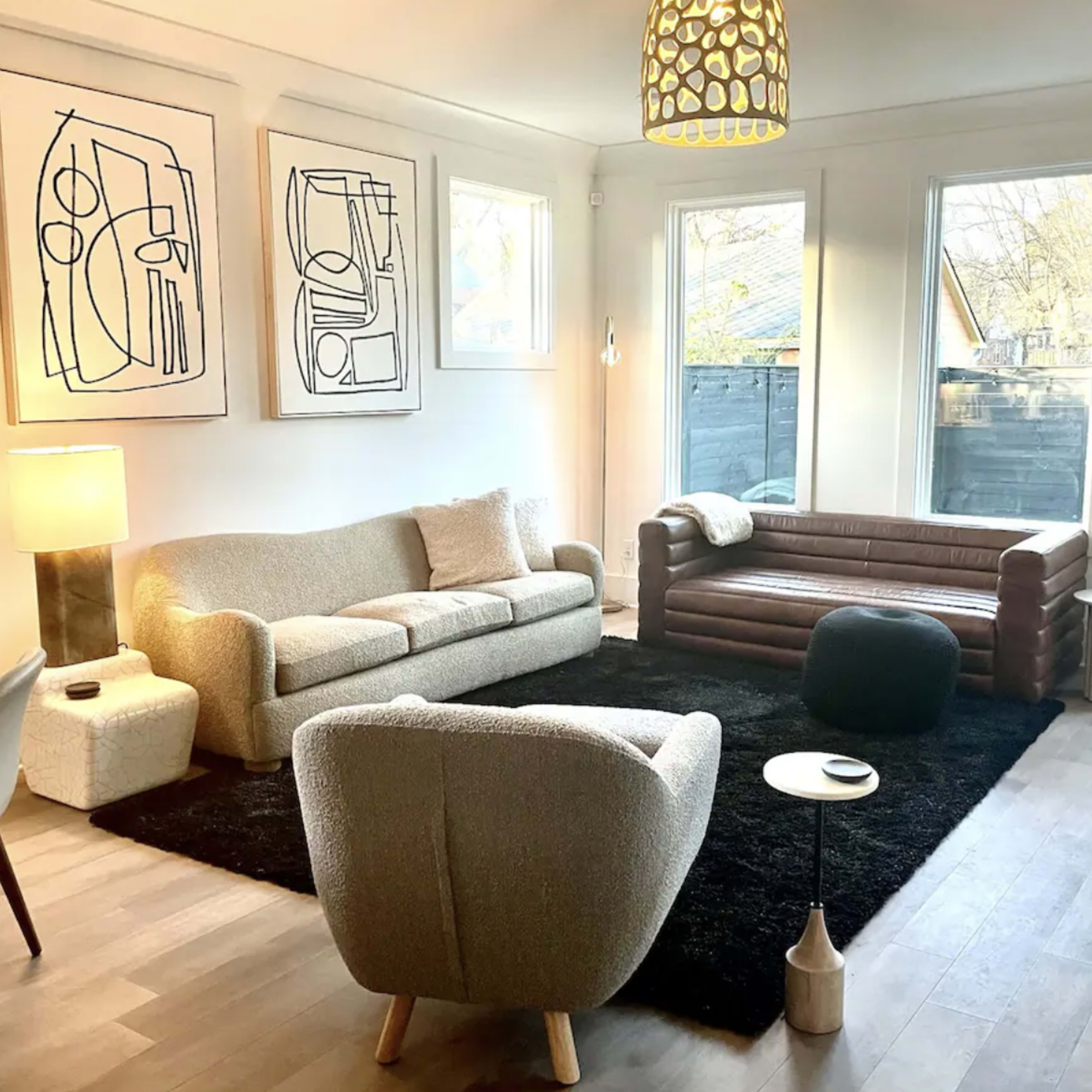 A modern living room featuring two sofas, a round coffee table, a floor lamp, and large windows allowing natural light to fill the space.