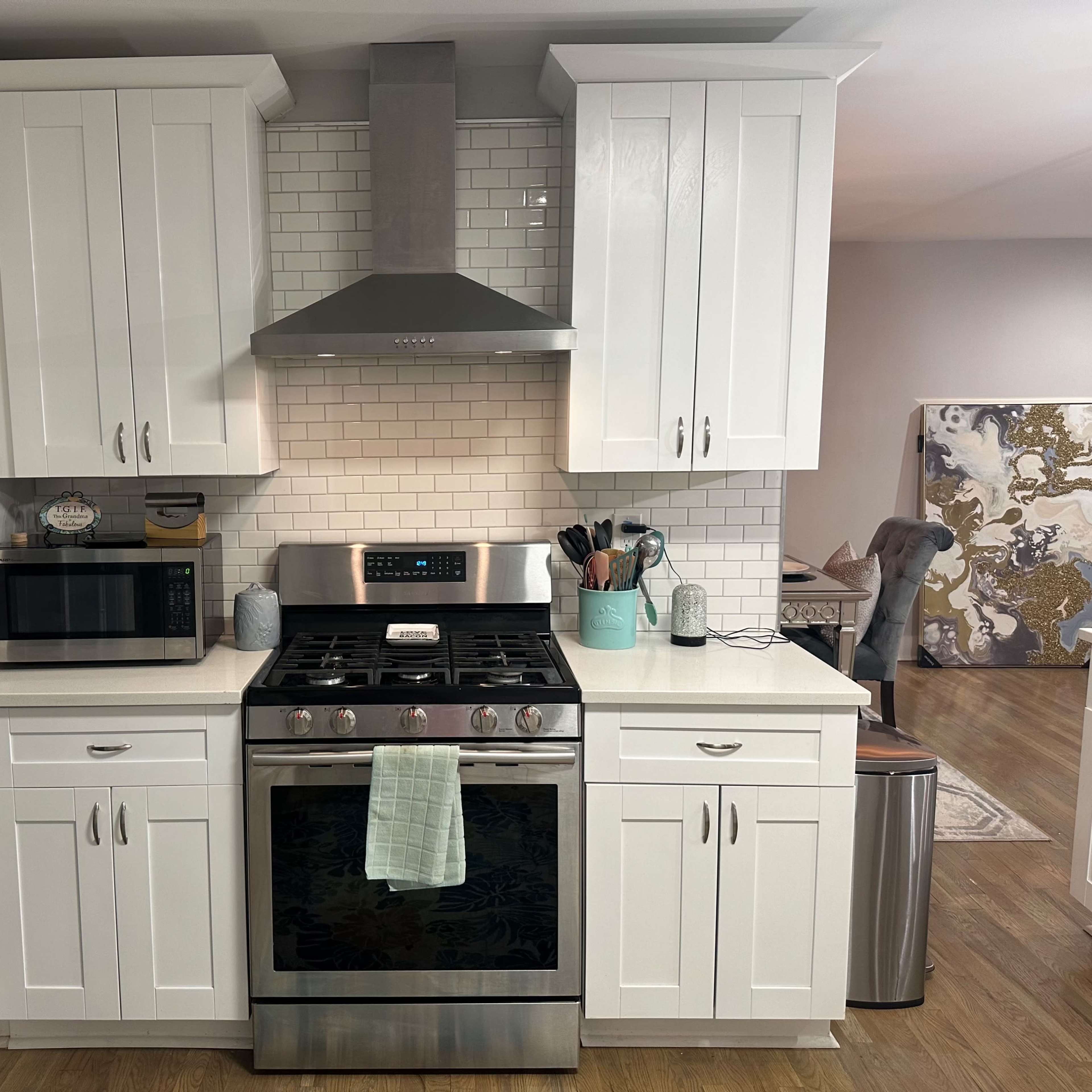 A modern kitchen with white cabinets, a stainless steel stove, a hood above the stove, and a microwave, all set against a tiled backsplash.
