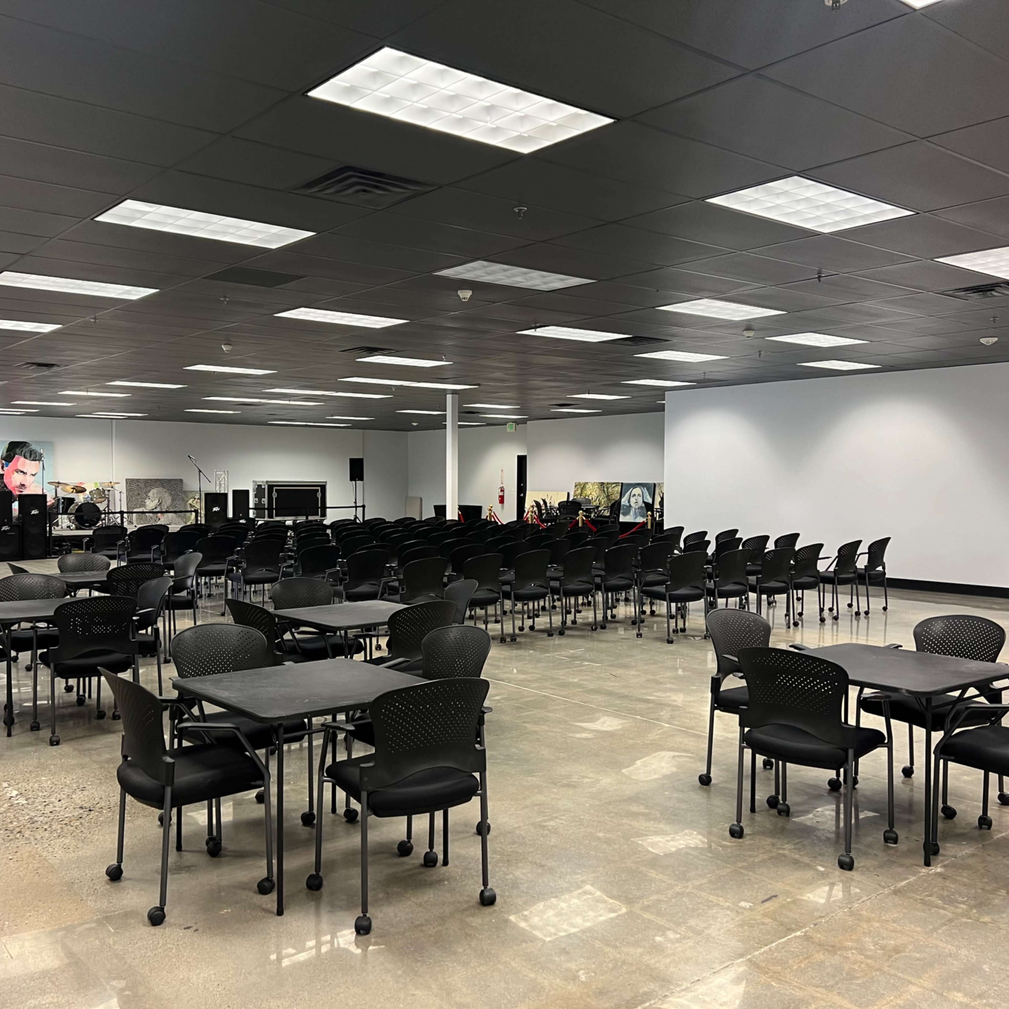 A spacious room filled with rows of black chairs and tables arranged for a gathering.