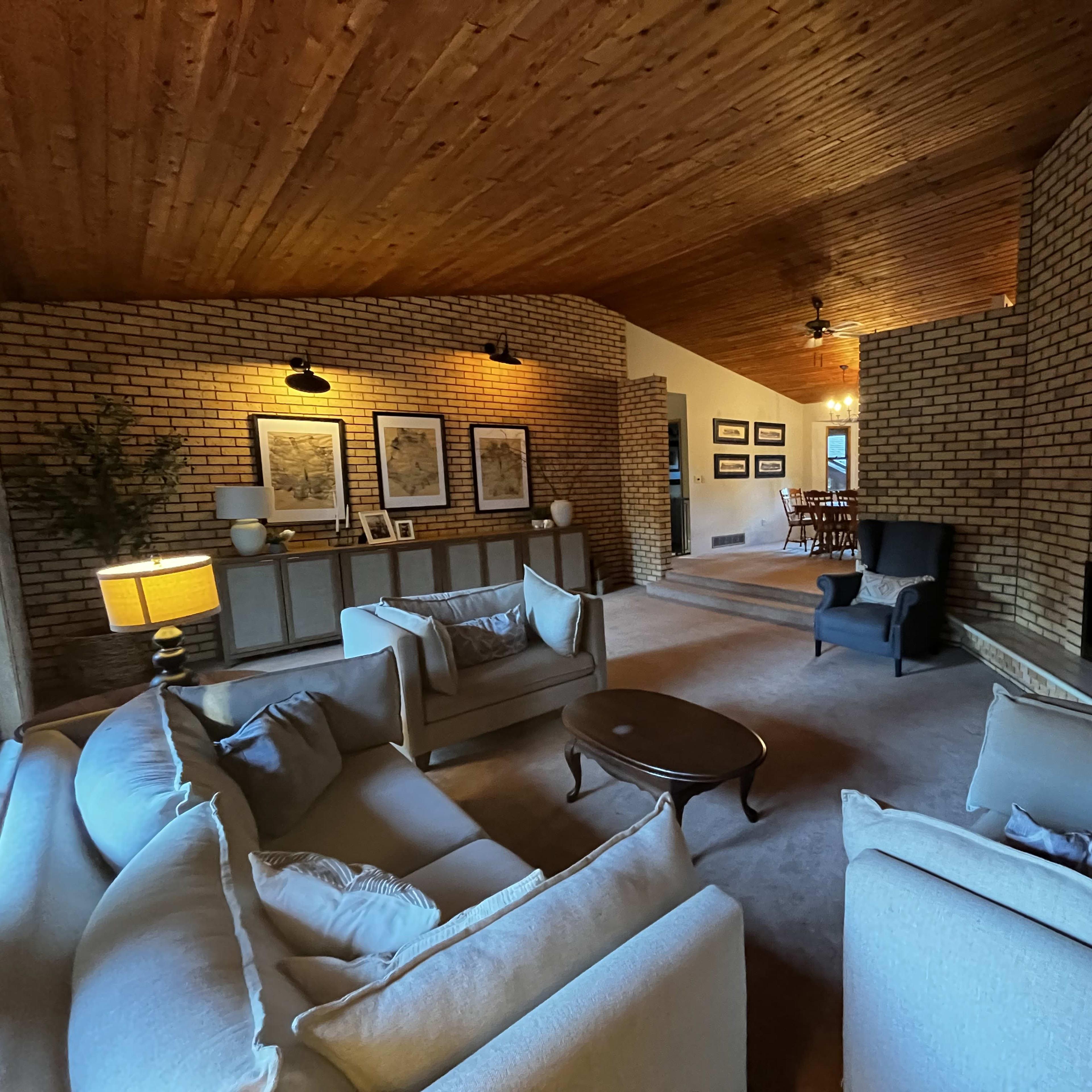 The living room features a high wooden ceiling, brick walls, a fireplace, and two sofas facing a coffee table.