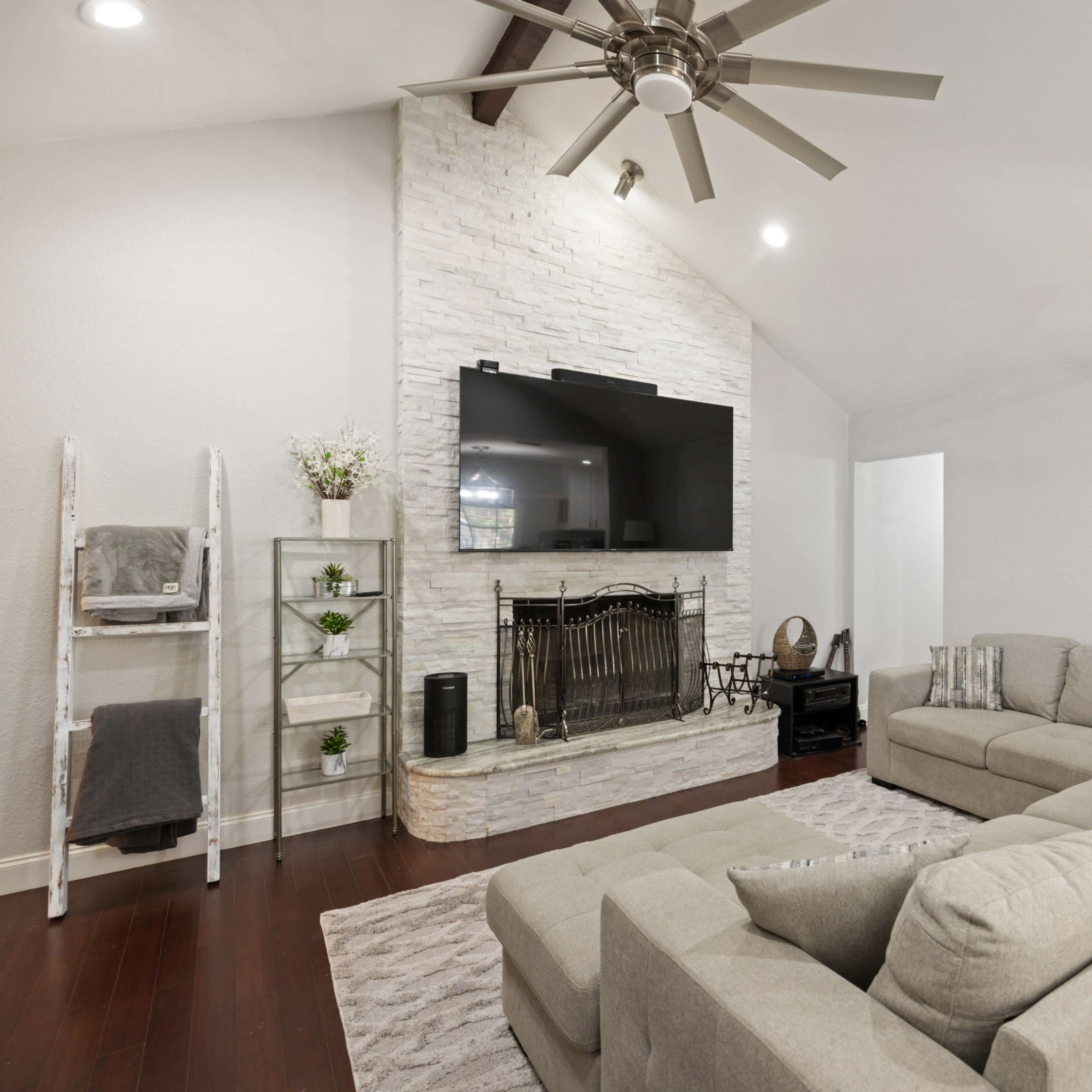 The living room features a spacious sectional couch facing a stone fireplace with a mounted flat-screen TV above it.