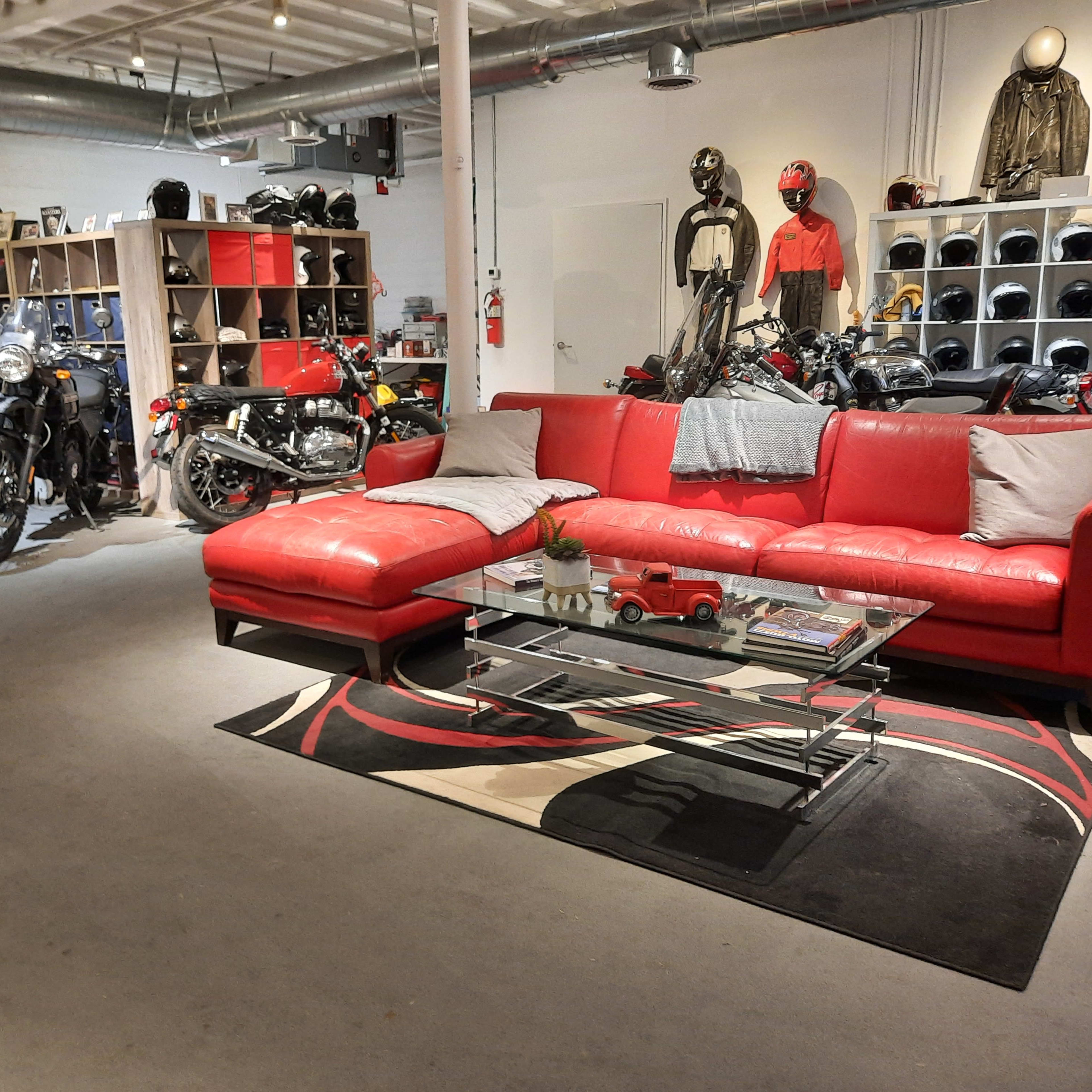 A spacious room with a red sectional sofa, glass coffee table, and shelves displaying motorcycles and helmets in the background.