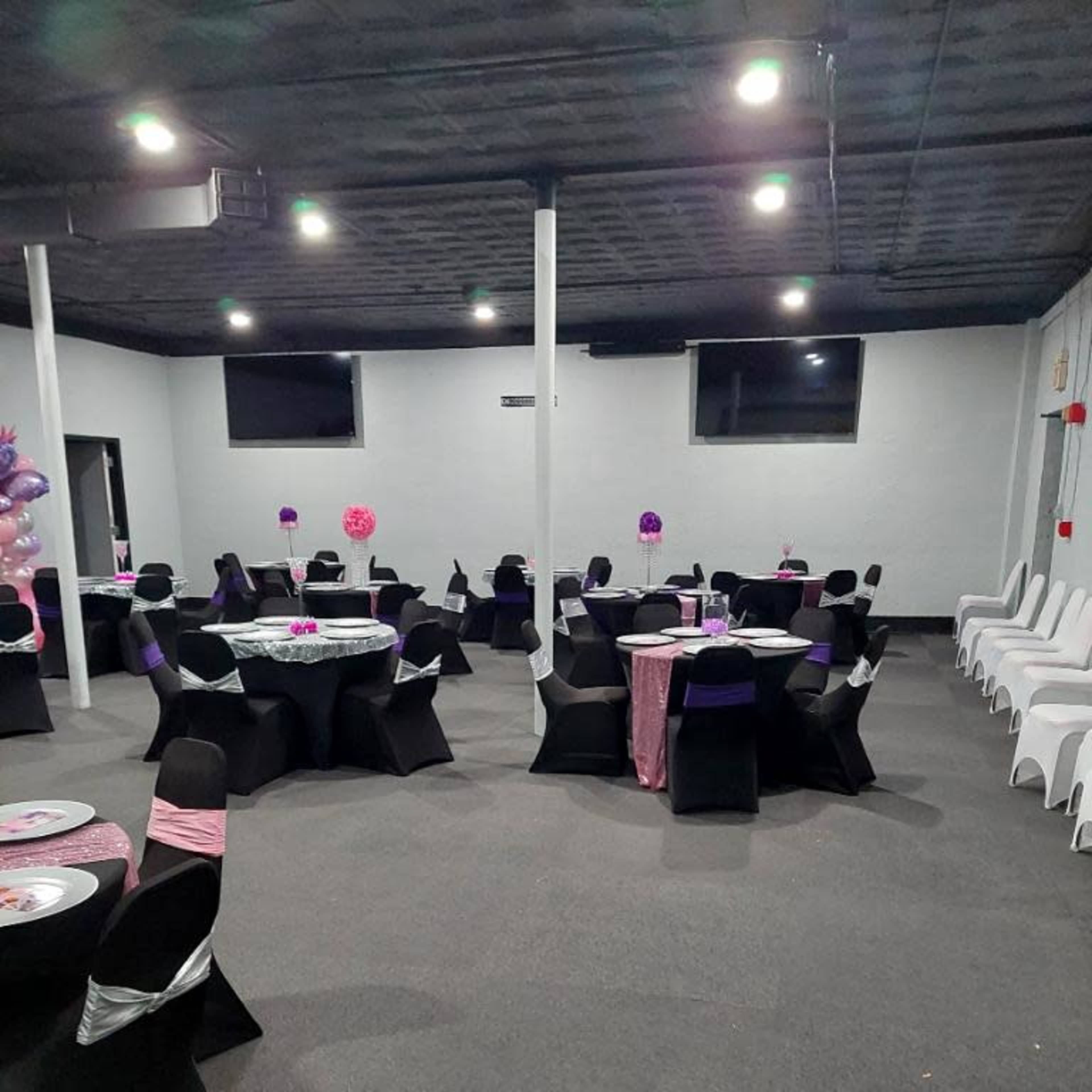 A party venue with several round tables set with black and pink decorations, surrounded by black and white chairs.
